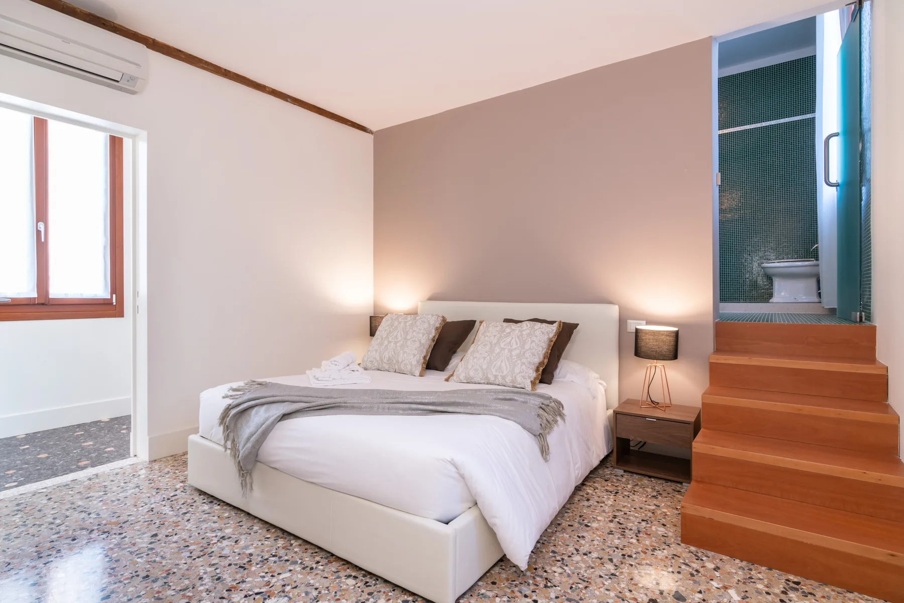 A bedroom with a neatly made bed and wooden steps beside it.