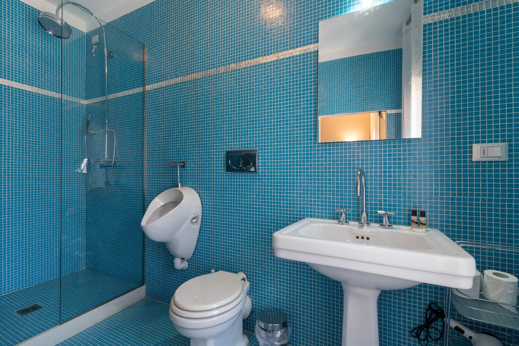 Un baño con azulejos azules, ducha, inodoro y lavabo con pedestal.