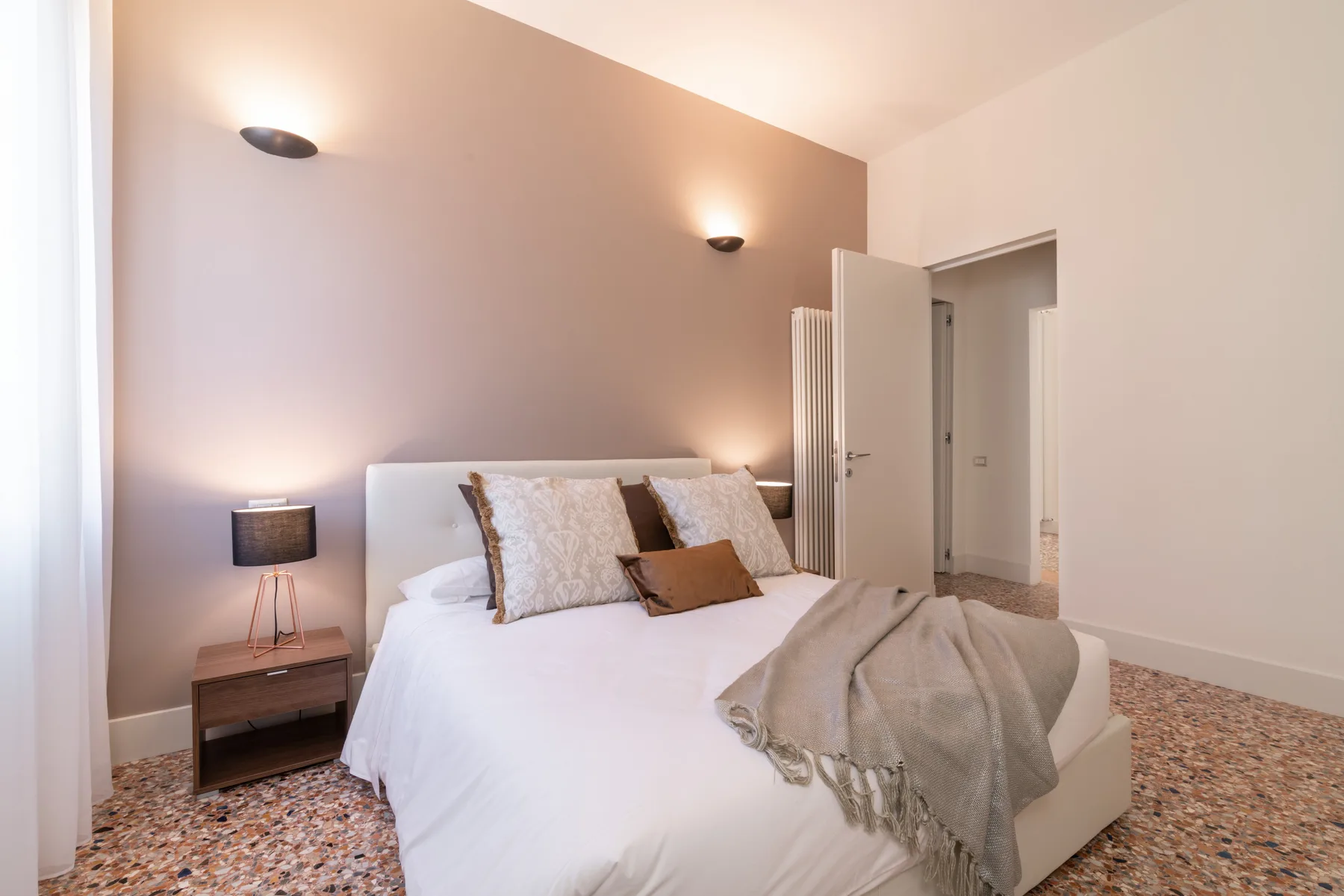 A bright bedroom with a neatly made bed and an open doorway.