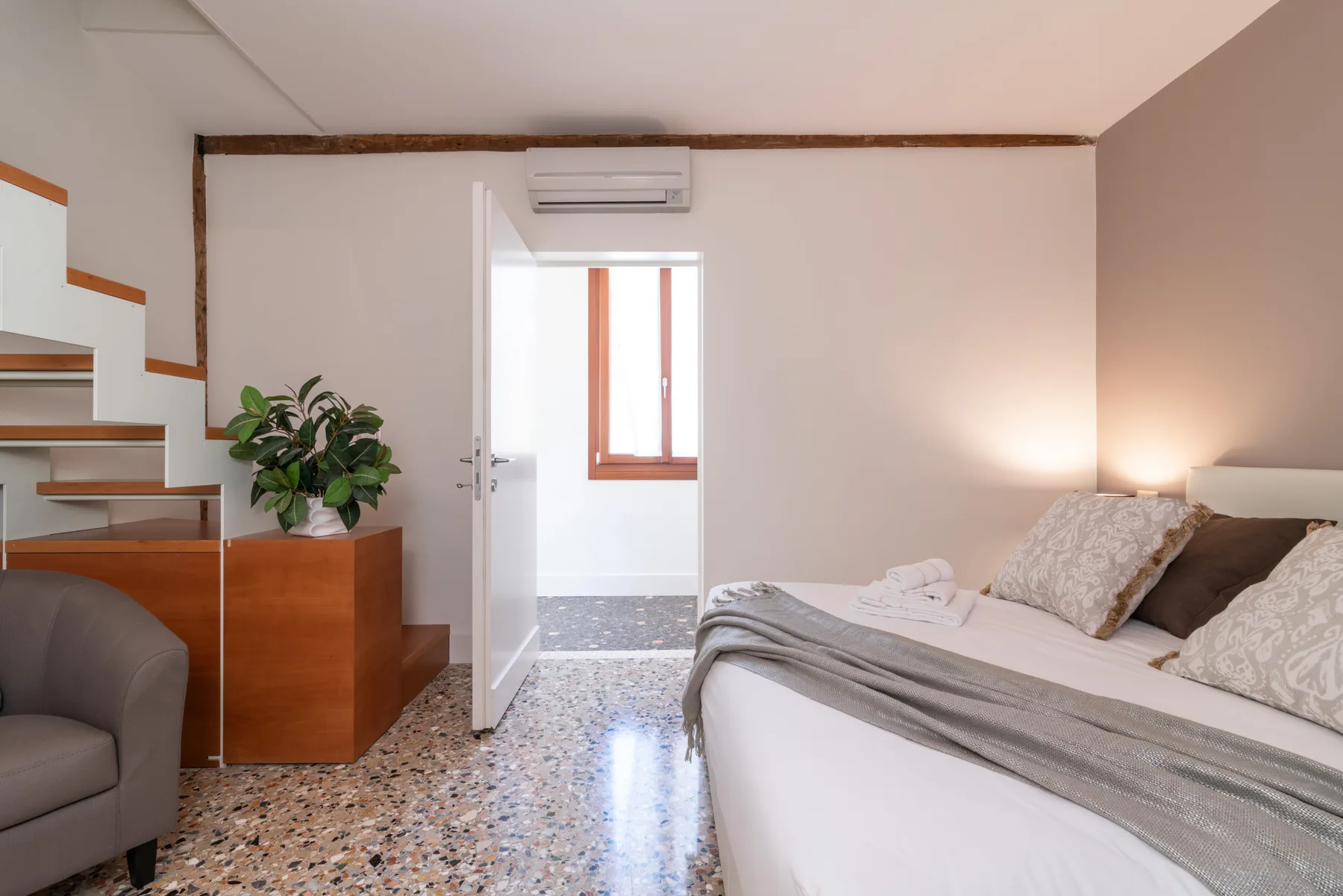 Un dormitorio con una cama, una puerta abierta y escaleras junto a la pared.