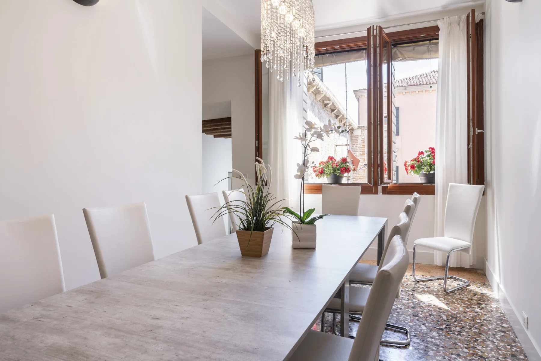 Un comedor luminoso con una mesa larga y ventanas abiertas.