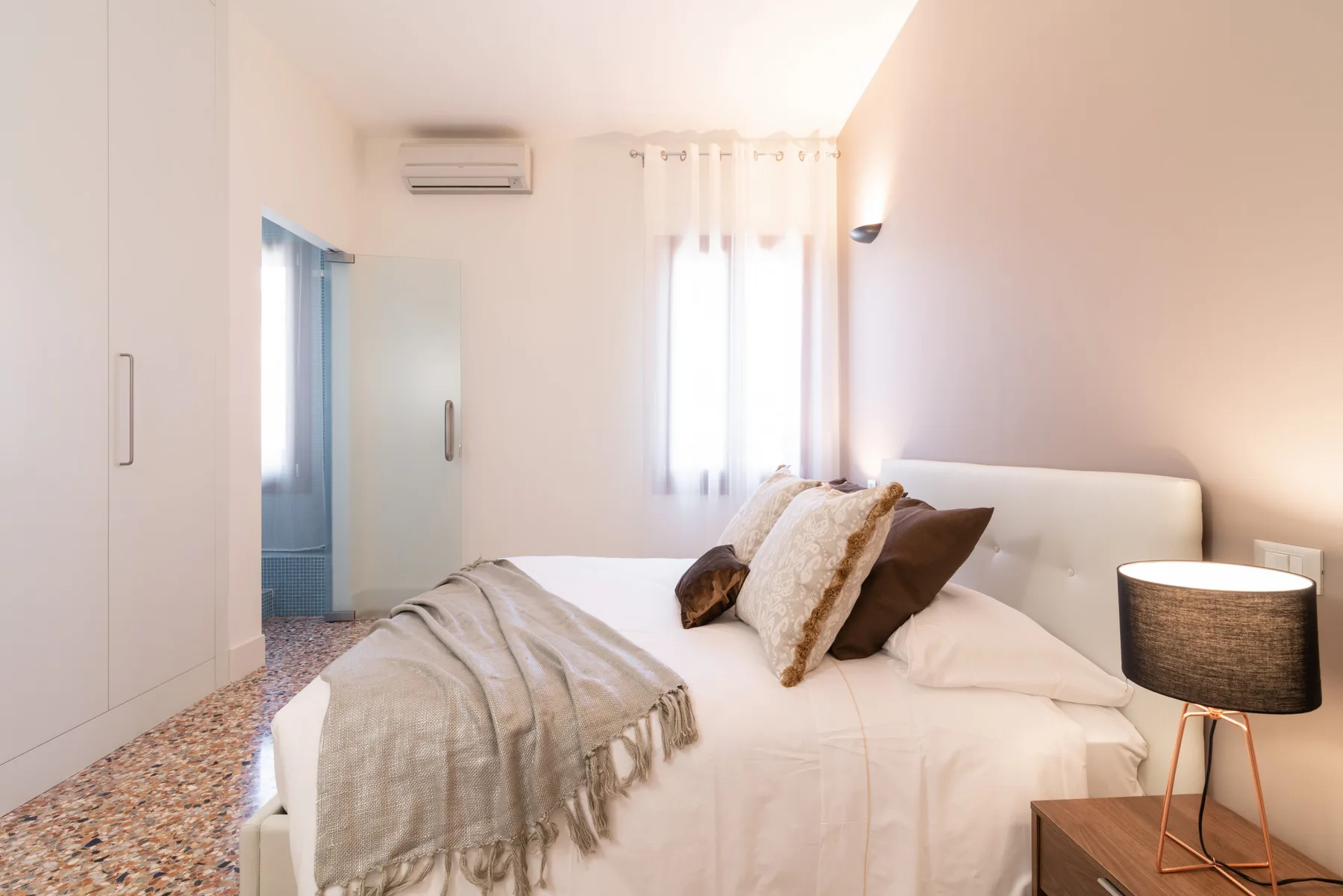 Un dormitorio luminoso con una cama tendida y cortinas translúcidas.