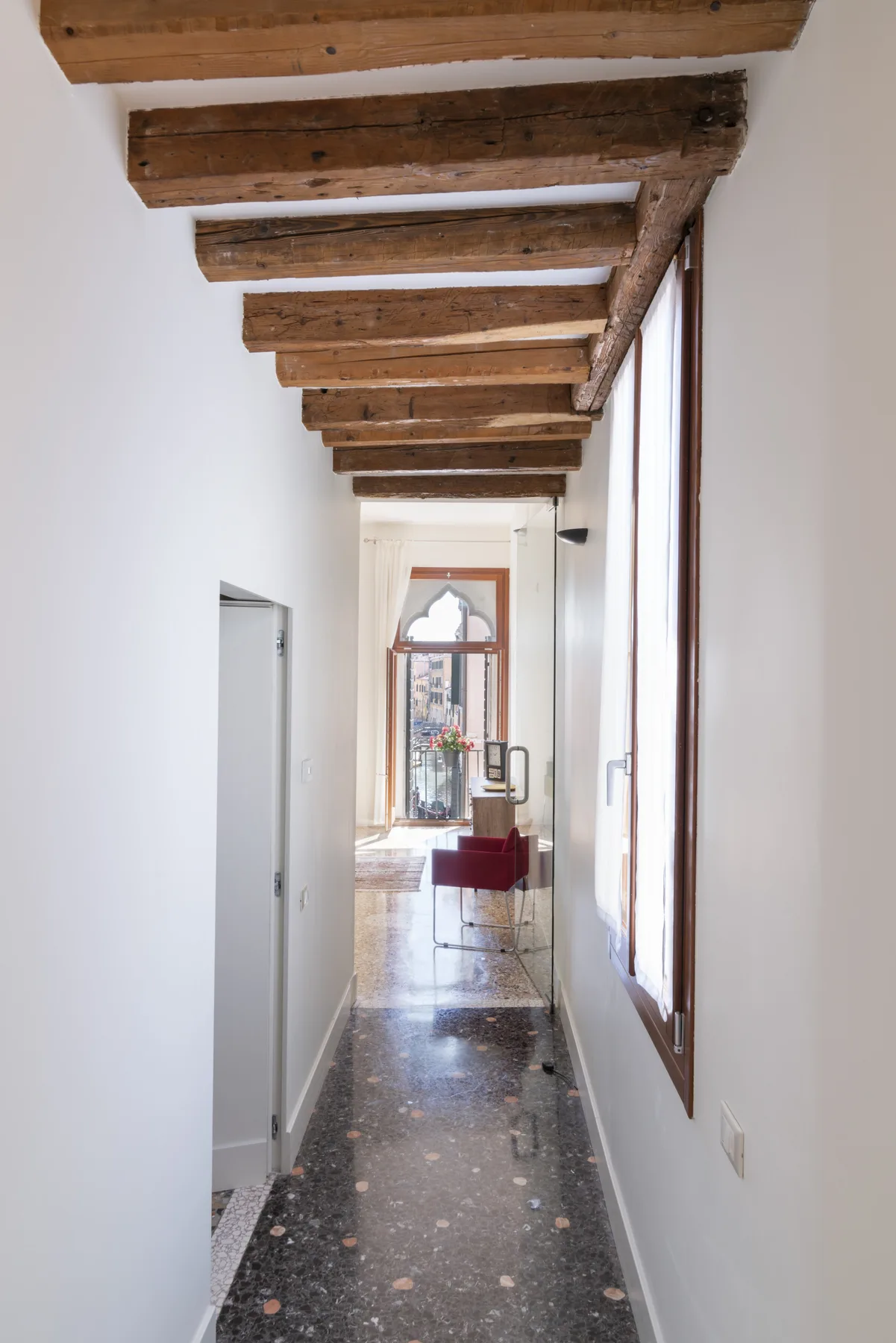 Un pasillo estrecho con vigas de madera expuestas y ventanas altas.