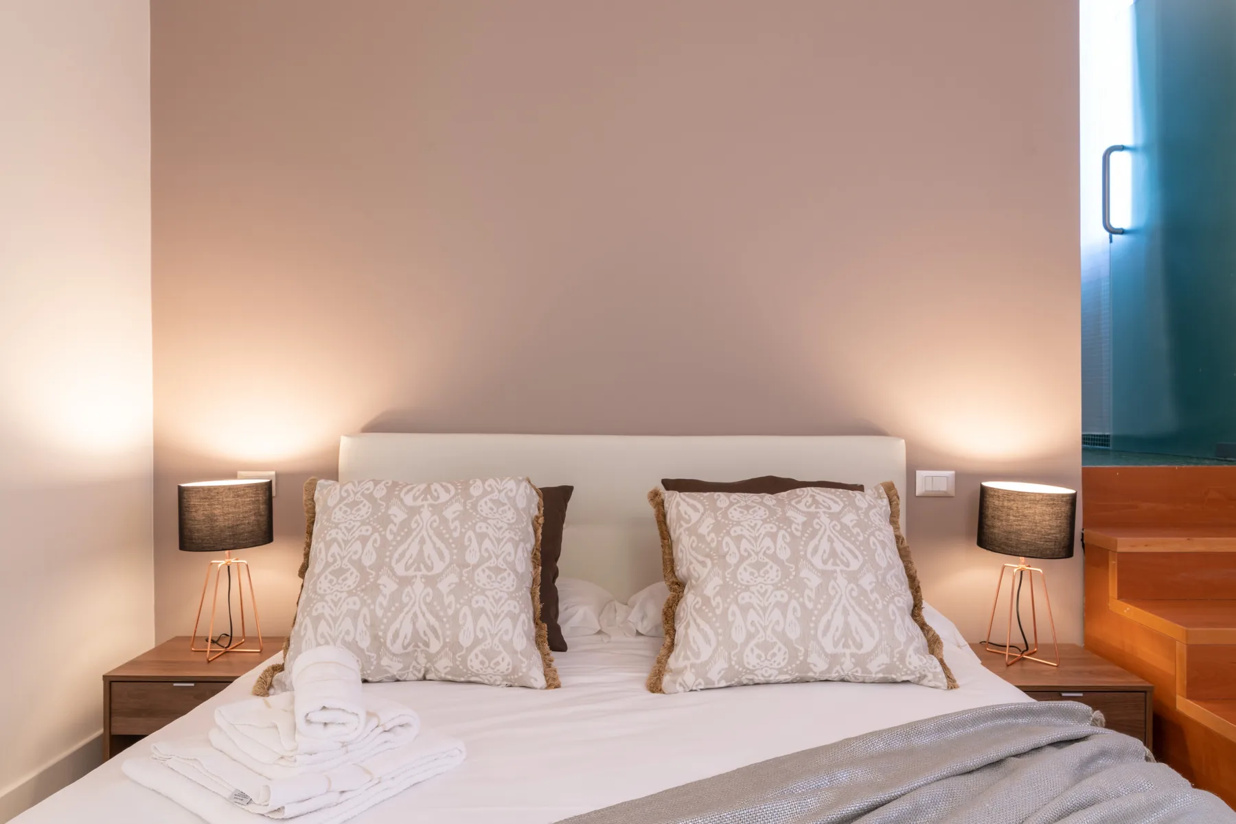 Dormitorio con una cama tendida, almohadas estampadas y lámparas de noche.