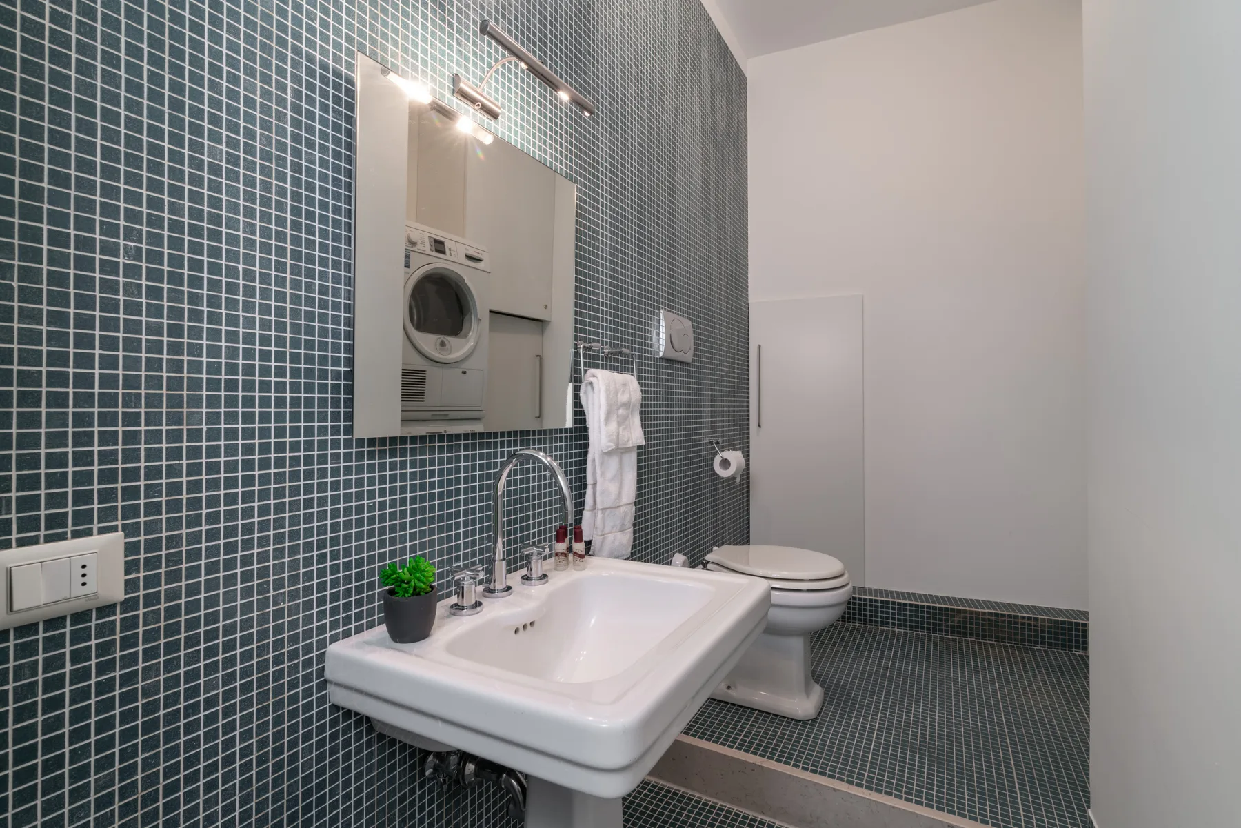 Un baño revestido de azulejos con lavabo, espejo e inodoro.