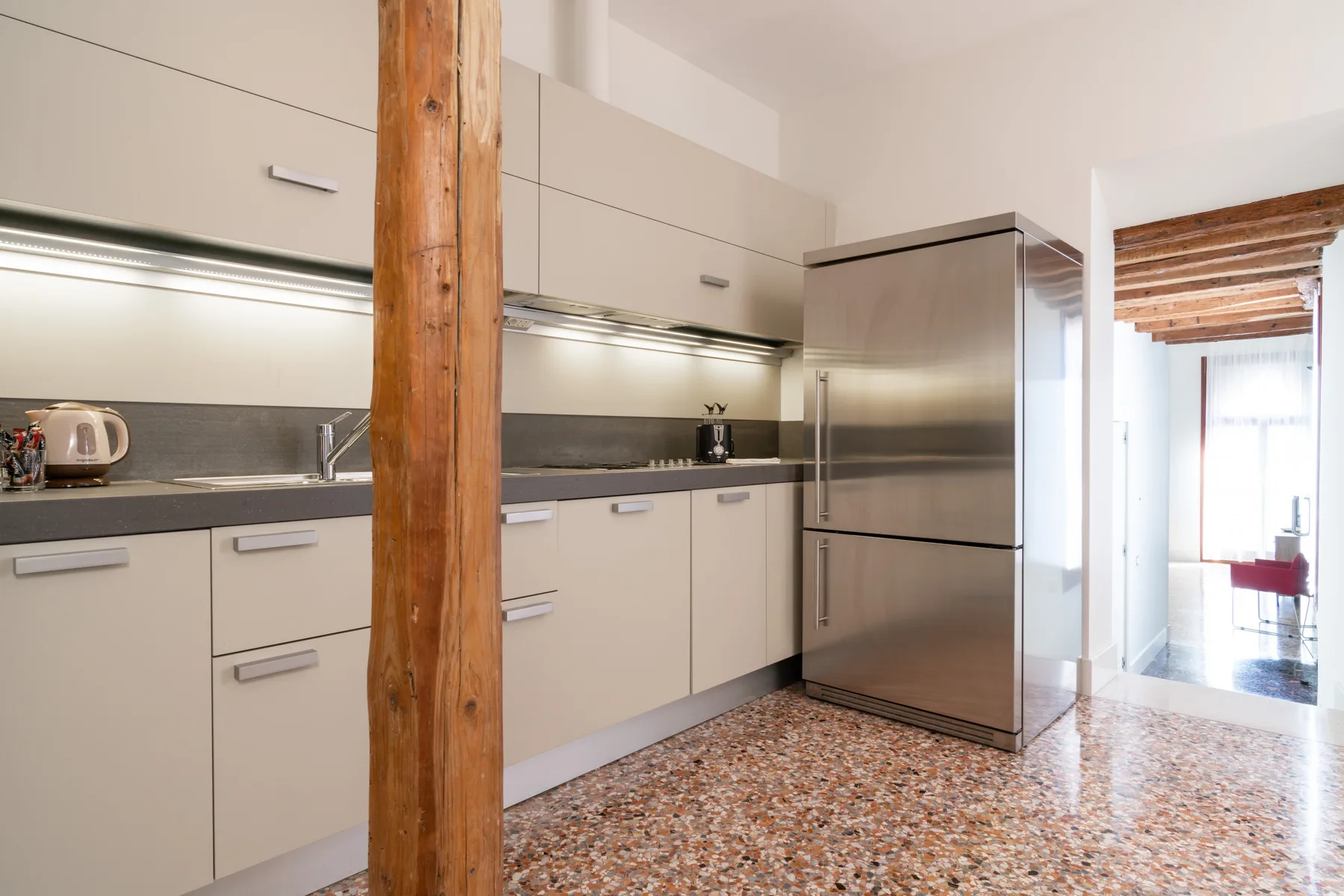 A bright kitchen with pale cabinets, a stainless-steel refrigerator, and a wooden support post.