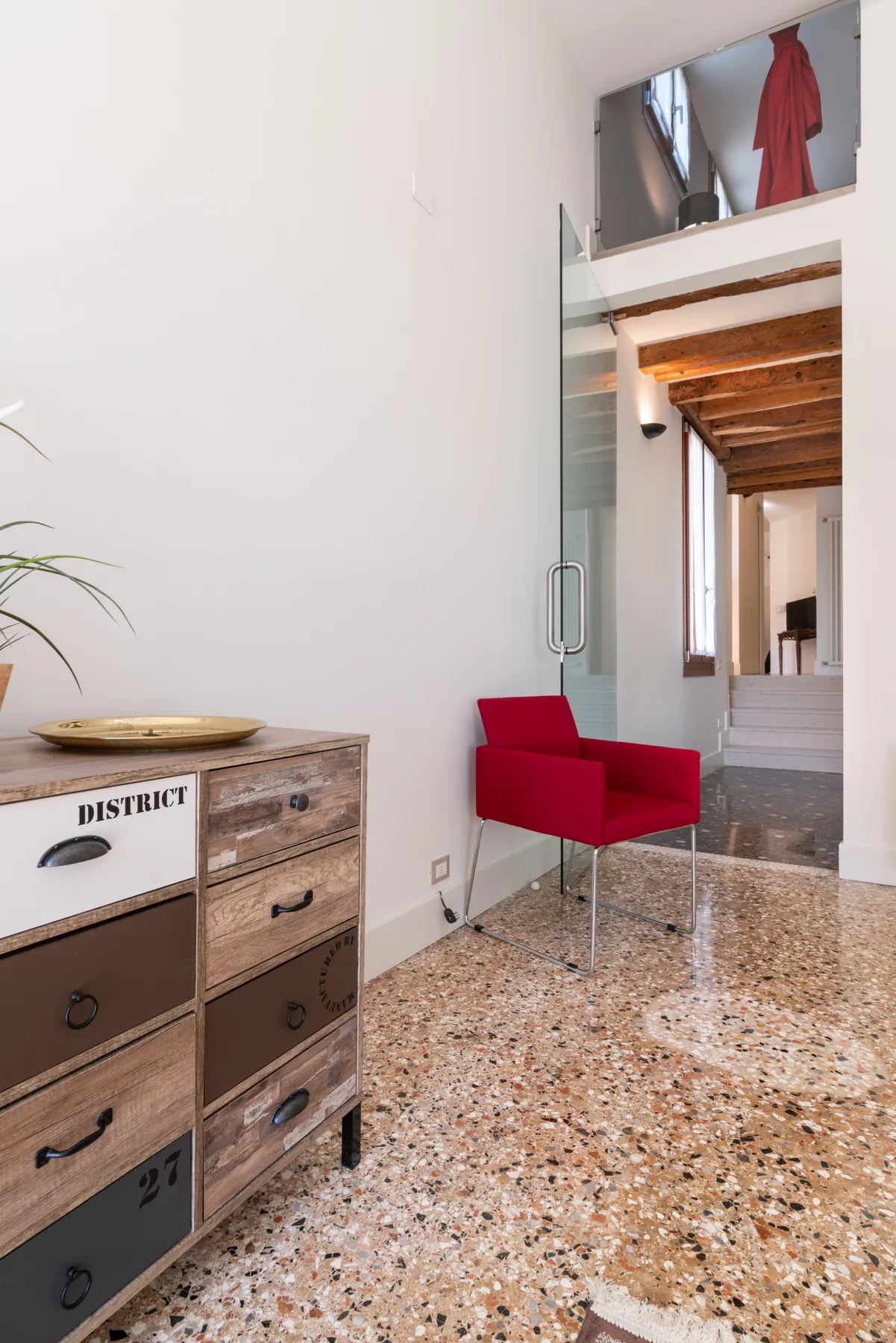 Un pasillo interior luminoso con una silla roja junto a una puerta de vidrio.
