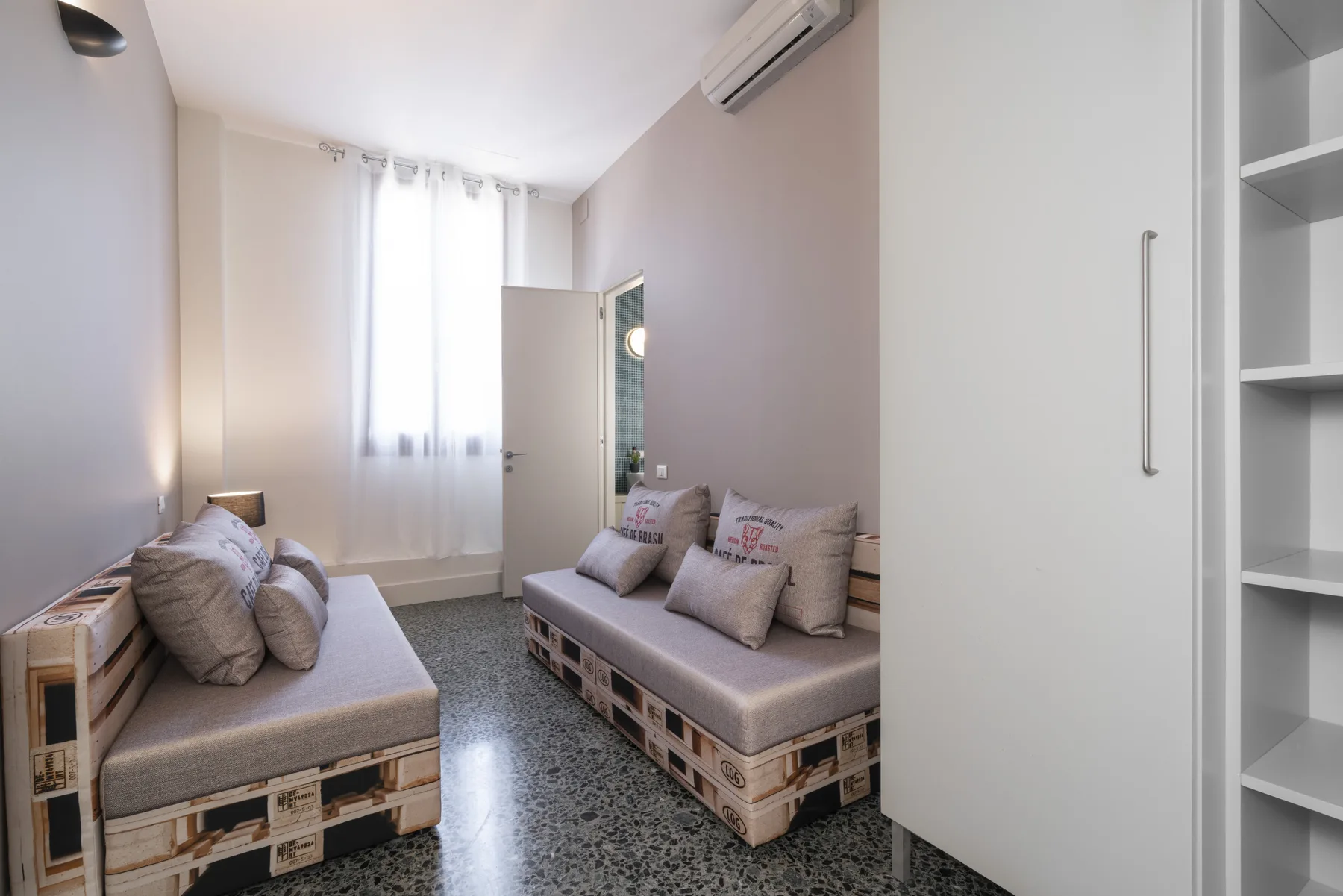 A compact bedroom with two cushioned beds and a bright window.