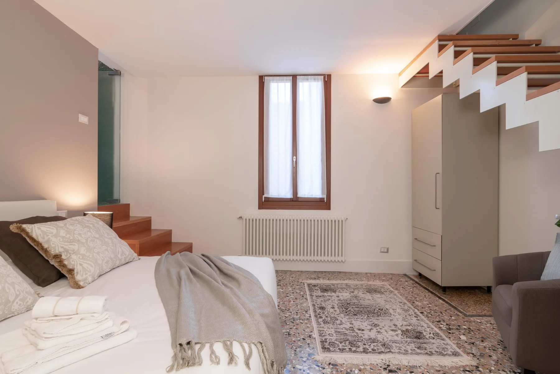 Un dormitorio con una cama, una ventana y una escalera a la derecha.