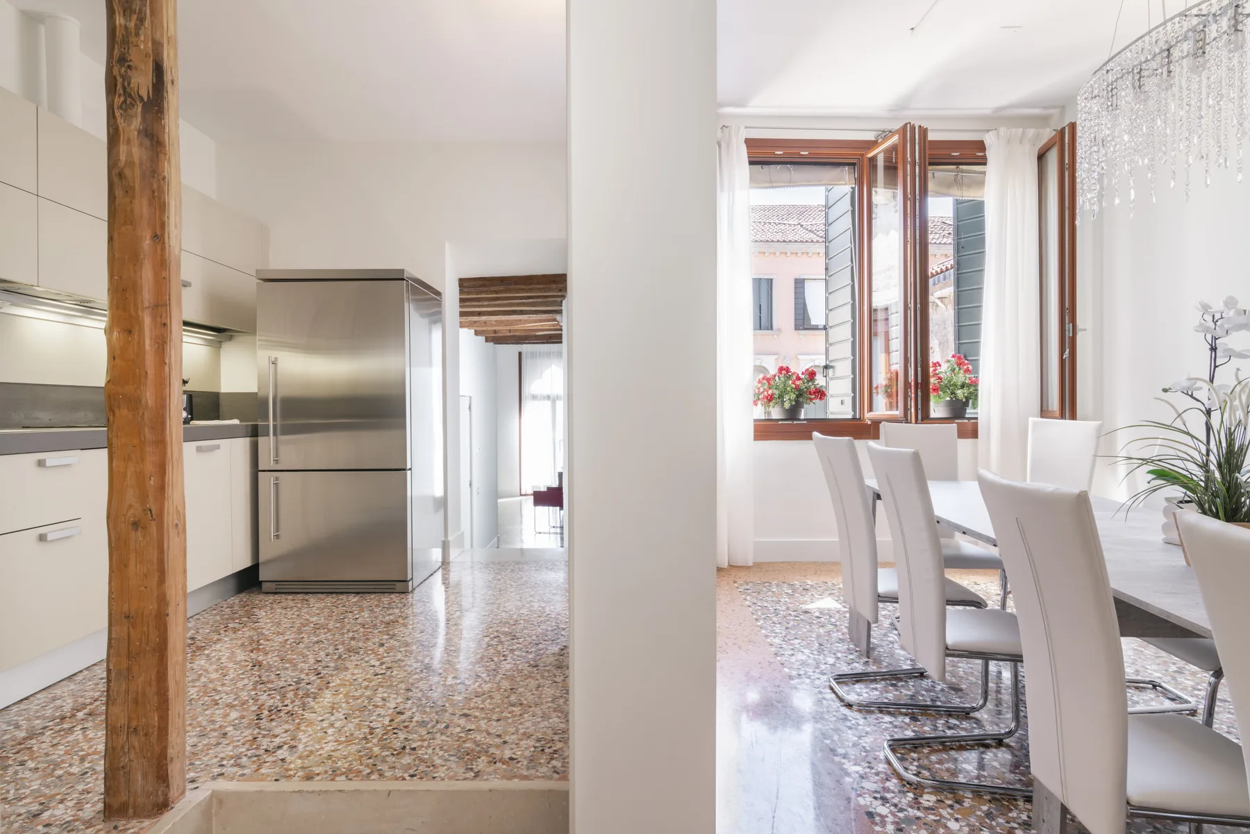 Una cocina abierta y zona de comedor con una mesa junto a ventanas altas.