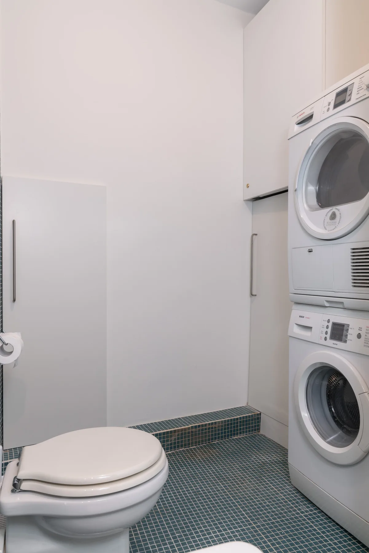 Un baño compacto con inodoro y lavadora y secadora apiladas.