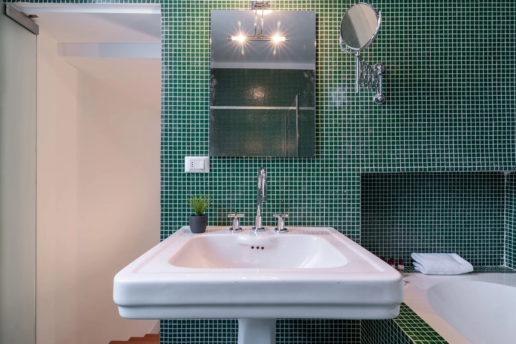 Un baño con un lavabo blanco y paredes de azulejos verdes.