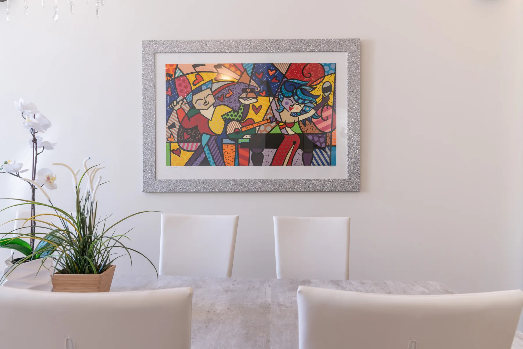 Un comedor con una mesa, asientos blancos y una obra colorida enmarcada en la pared.