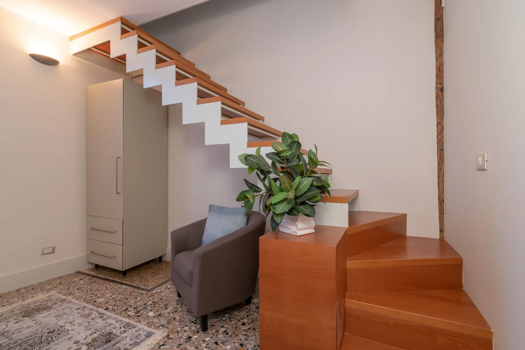 Una sala de estar con asientos junto a una escalera de madera y una planta en maceta.