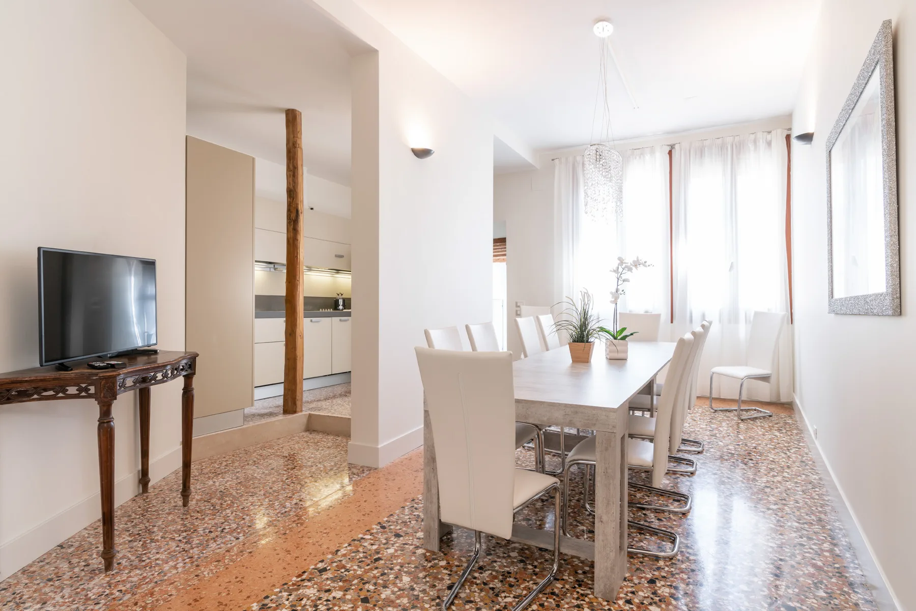Un comedor luminoso con una mesa larga y sillas junto a un televisor.