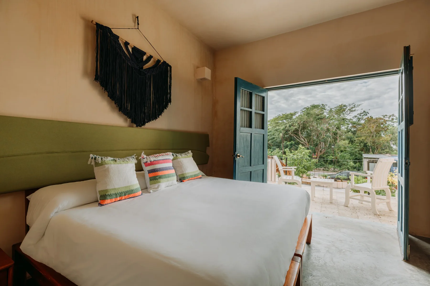 Habitación del Hotel WAYE en Valladolid con cama king, cabecera verde, textiles artesanales y puertas abiertas al balcón con vista a la naturaleza