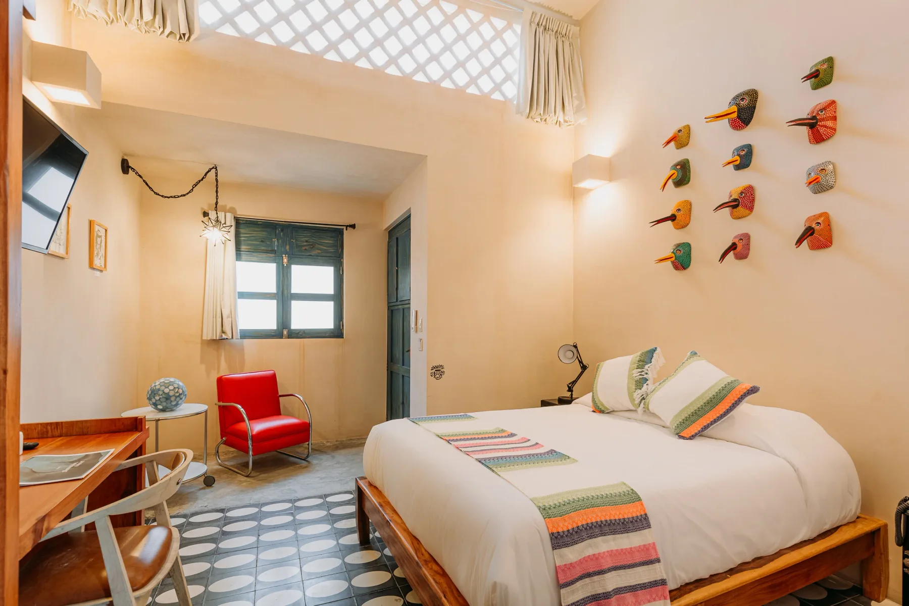 Habitación del Hotel WAYE en Valladolid con cama king, sillón rojo retro, máscaras de aves artesanales en la pared y piso de mosaico
