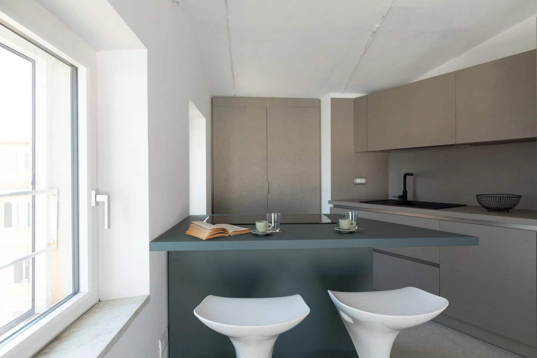 Una cocina moderna con una isla oscura y dos asientos blancos.