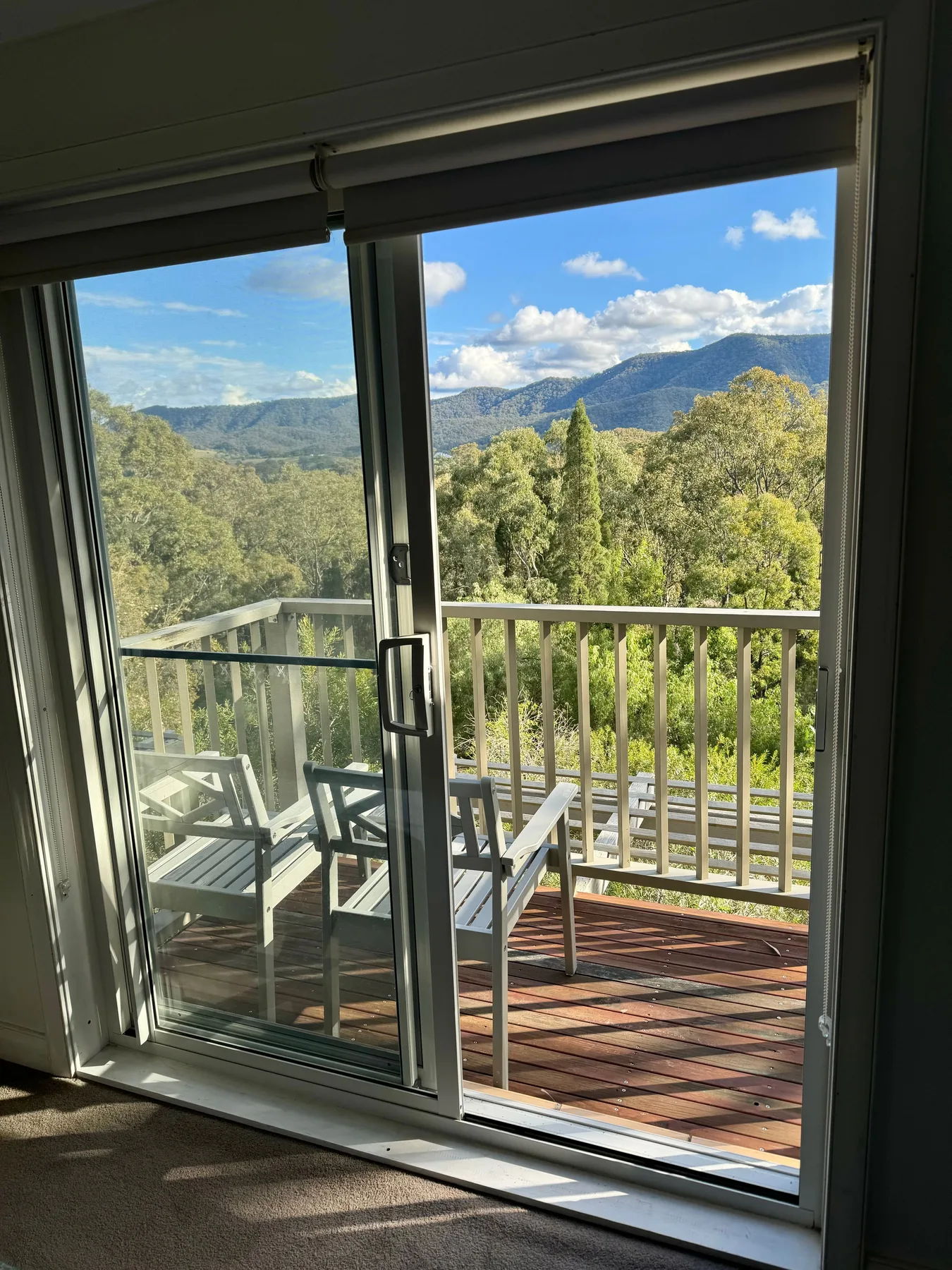 Una puerta corrediza de vidrio da a una terraza con vistas a colinas boscosas y montañas.
