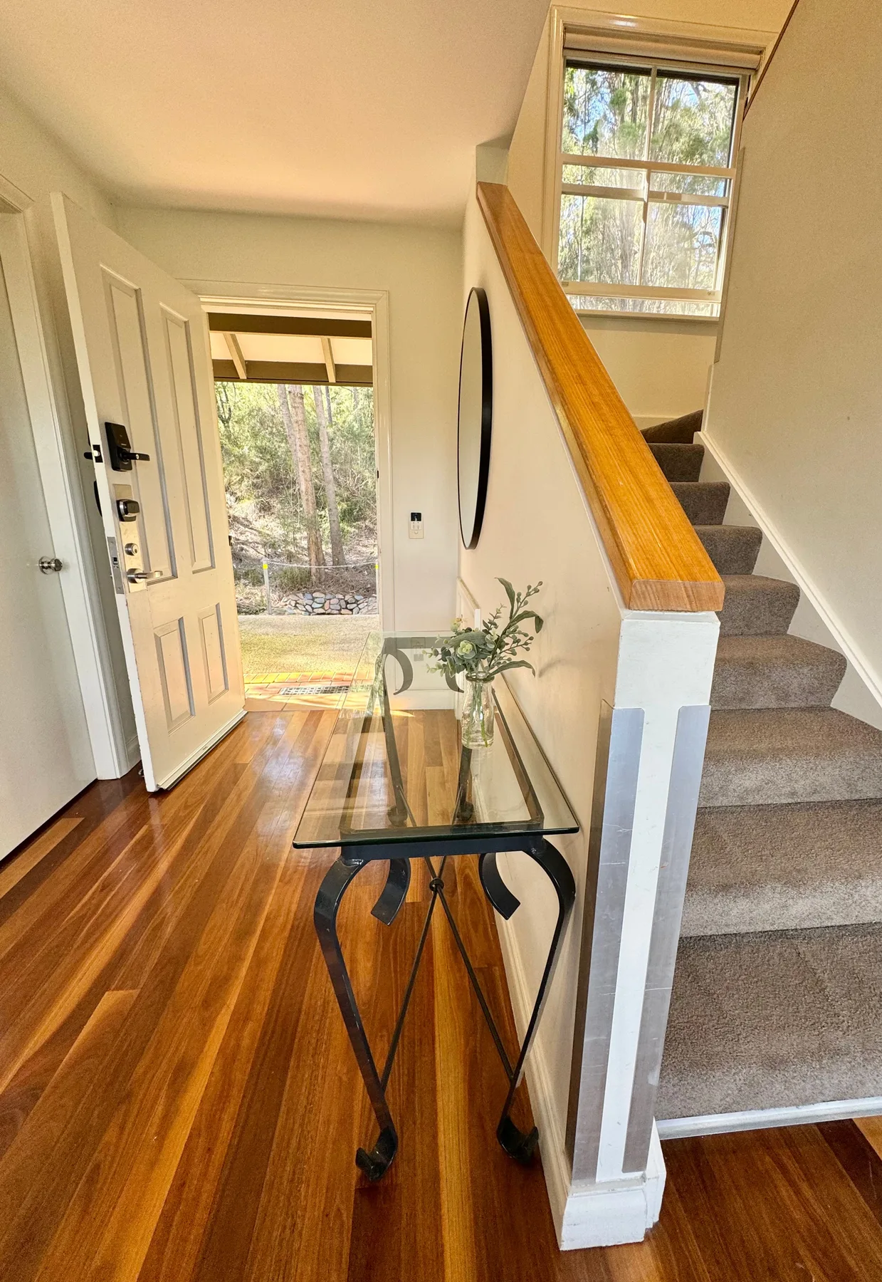 Un recibidor con una mesa de cristal junto a una escalera y una puerta abierta.