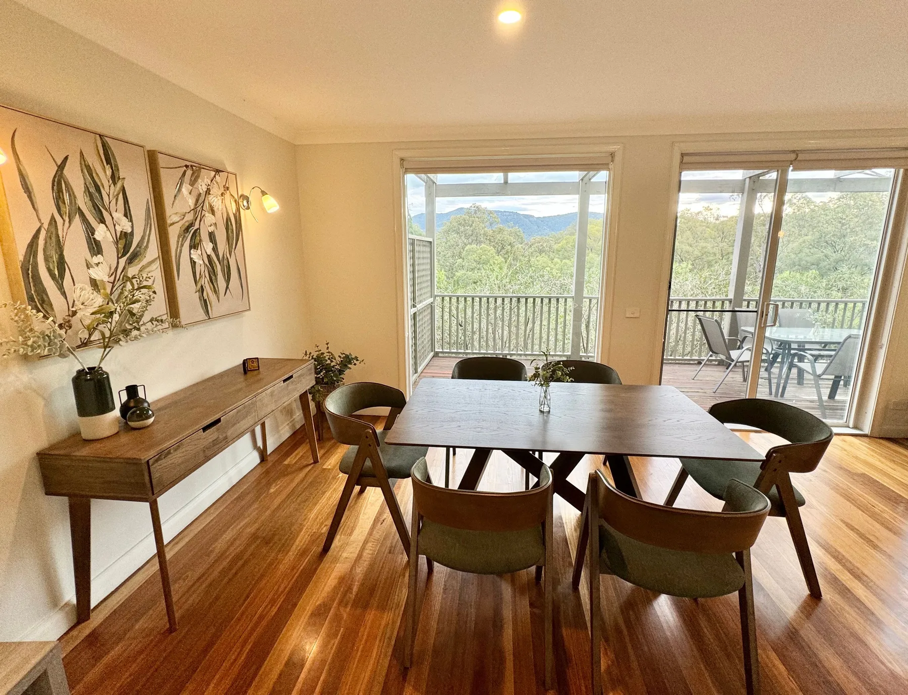 Comedor con mesa y sillas de madera junto a puertas de vidrio que dan a un balcón.