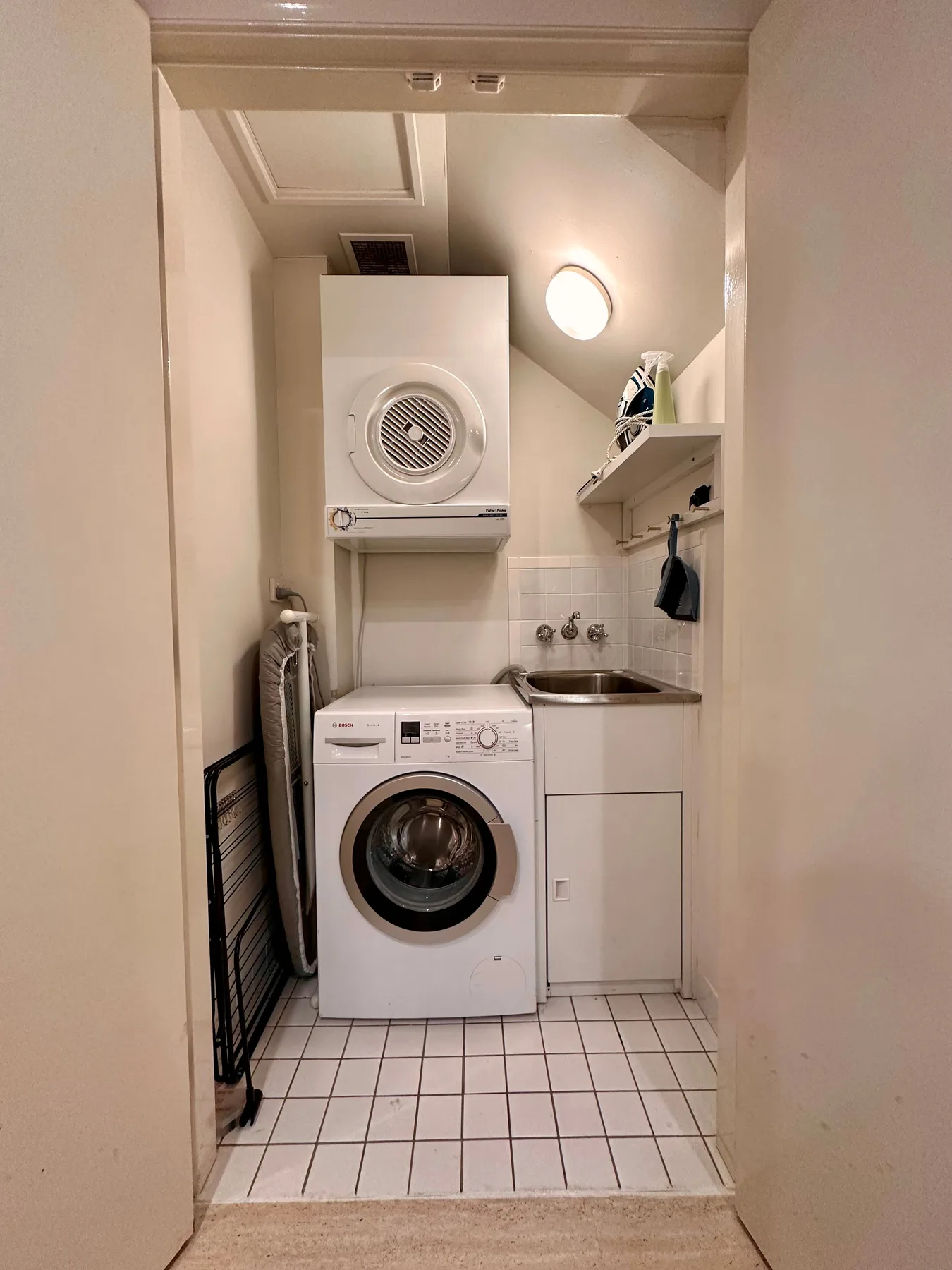 Un pequeño cuarto de lavandería con lavadora y secadora apiladas junto a un lavabo.
