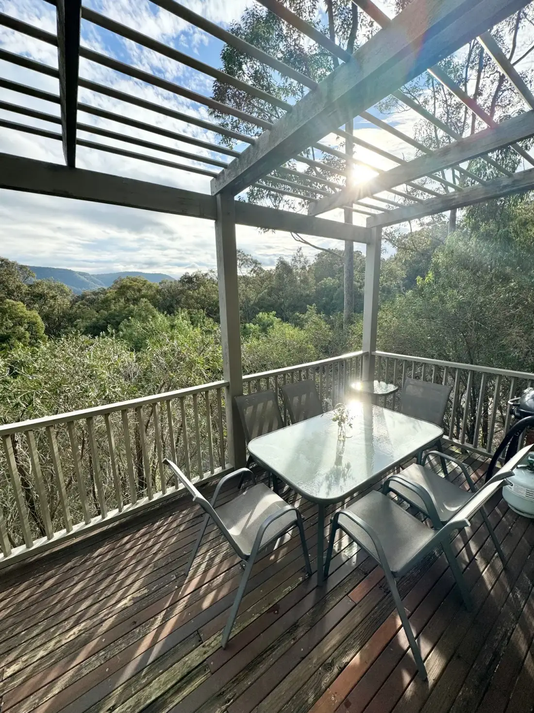Una terraza exterior cubierta con mesa y asientos da a colinas arboladas.