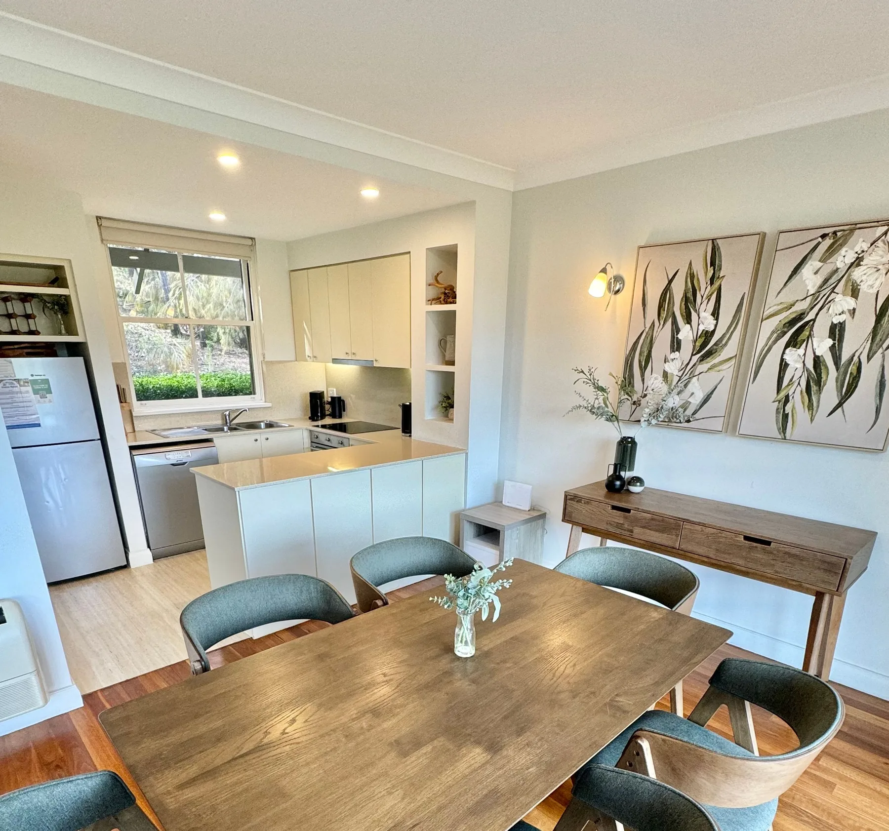 Una cocina luminosa con comedor, mesa de madera y gabinetes blancos.