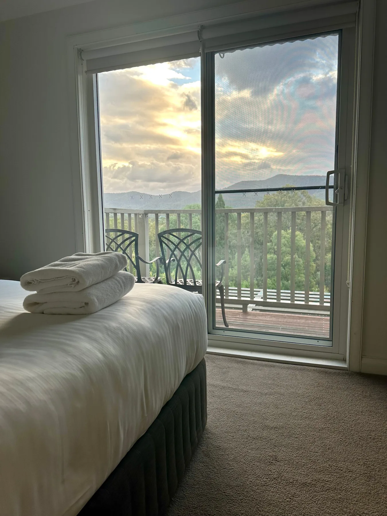 Un dormitorio con una cama junto a puertas de vidrio que dan a un balcón con vistas a las montañas.