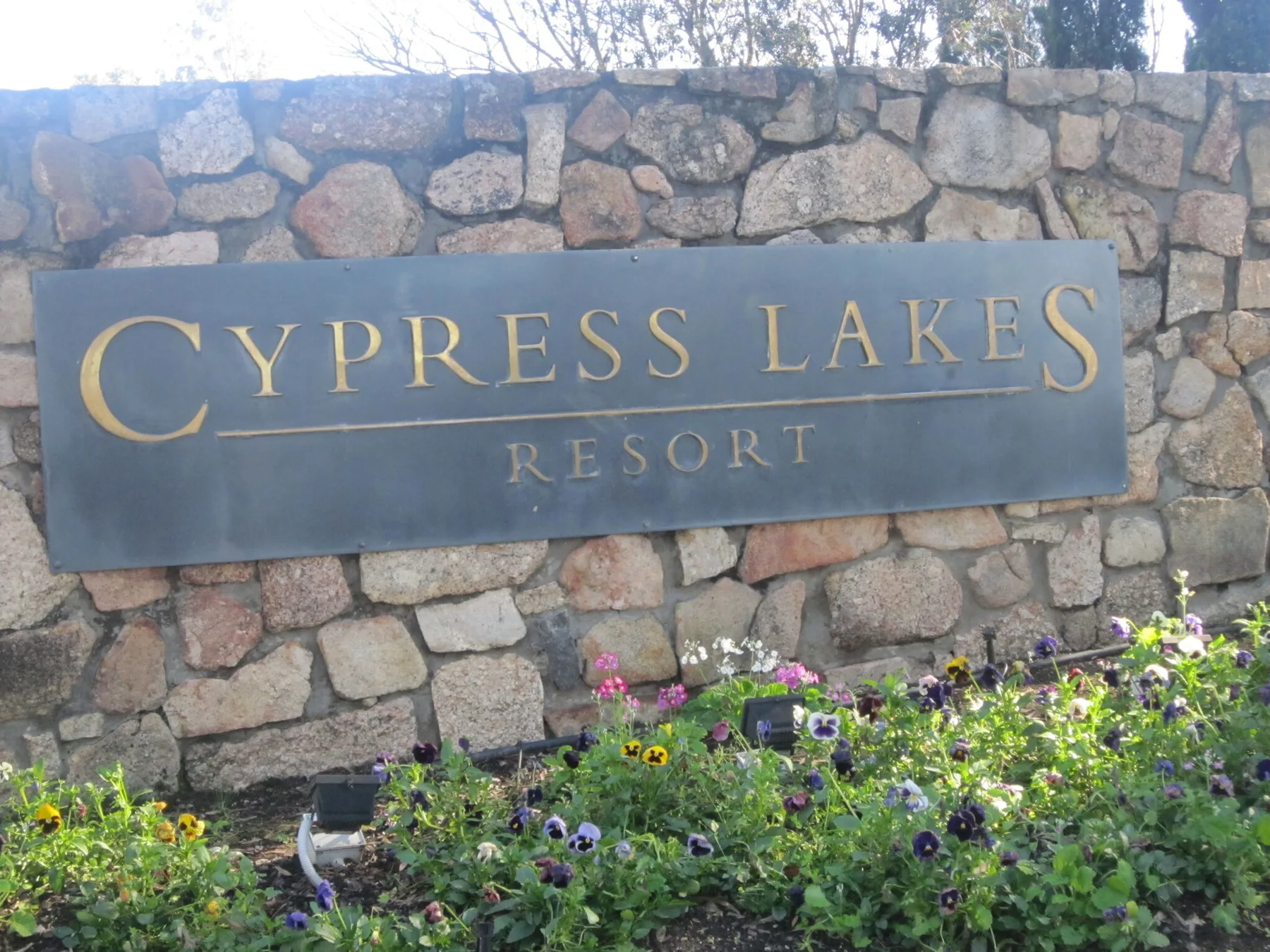 Un letrero de Cypress Lakes Resort está montado en un muro de piedra sobre flores.