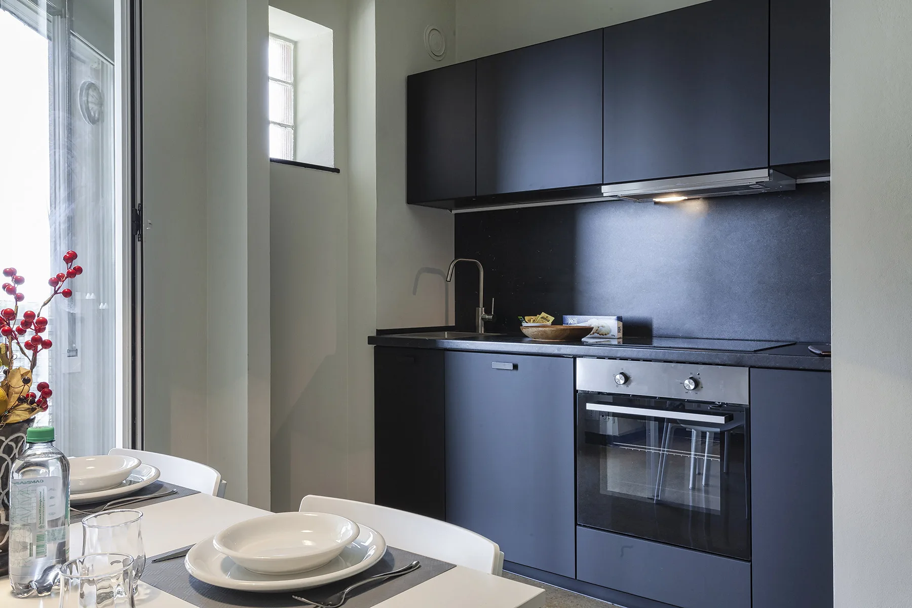 Una cocina moderna con gabinetes oscuros, un horno y una mesa de comedor junto a la ventana.