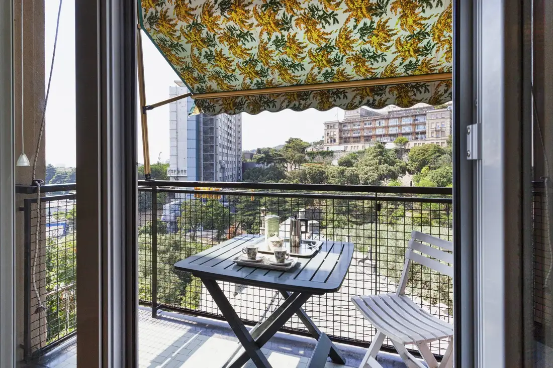 Una zona de estar en un balcón con mesa y sillas bajo un toldo estampado.
