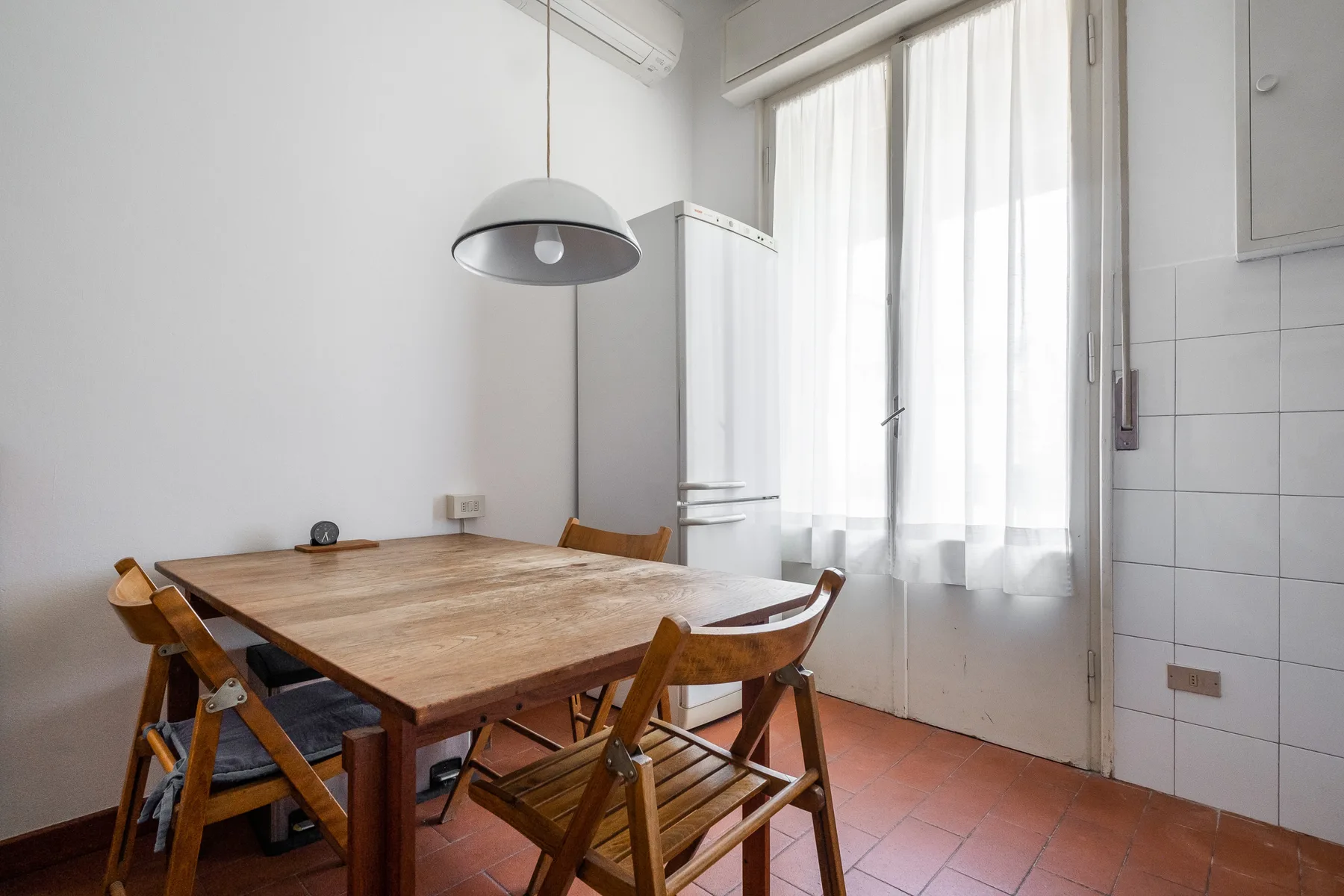 A dining area with a wooden table and seating beside tall curtained windows.