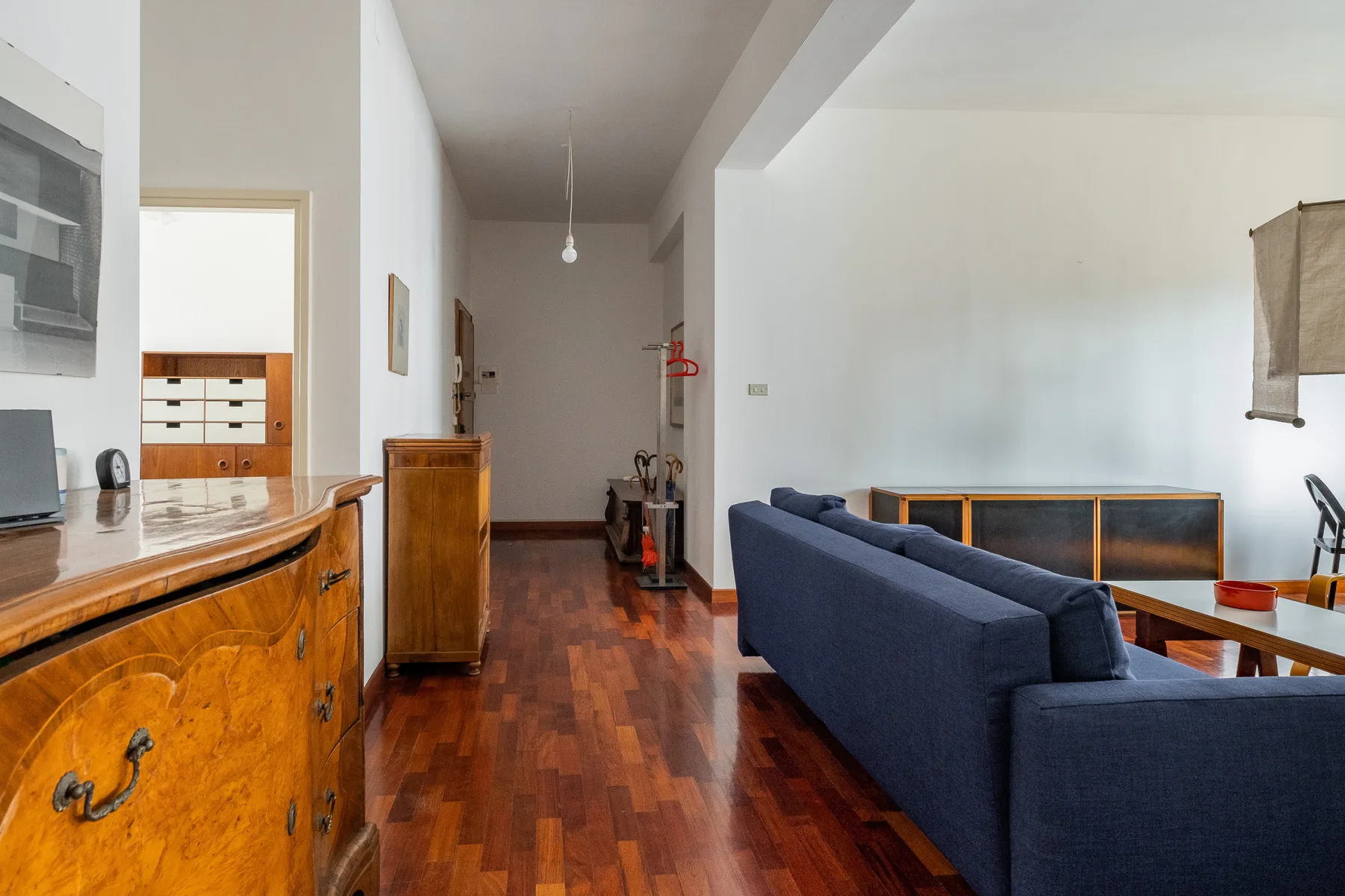 A living room with blue seating beside a wooden sideboard and a hallway.