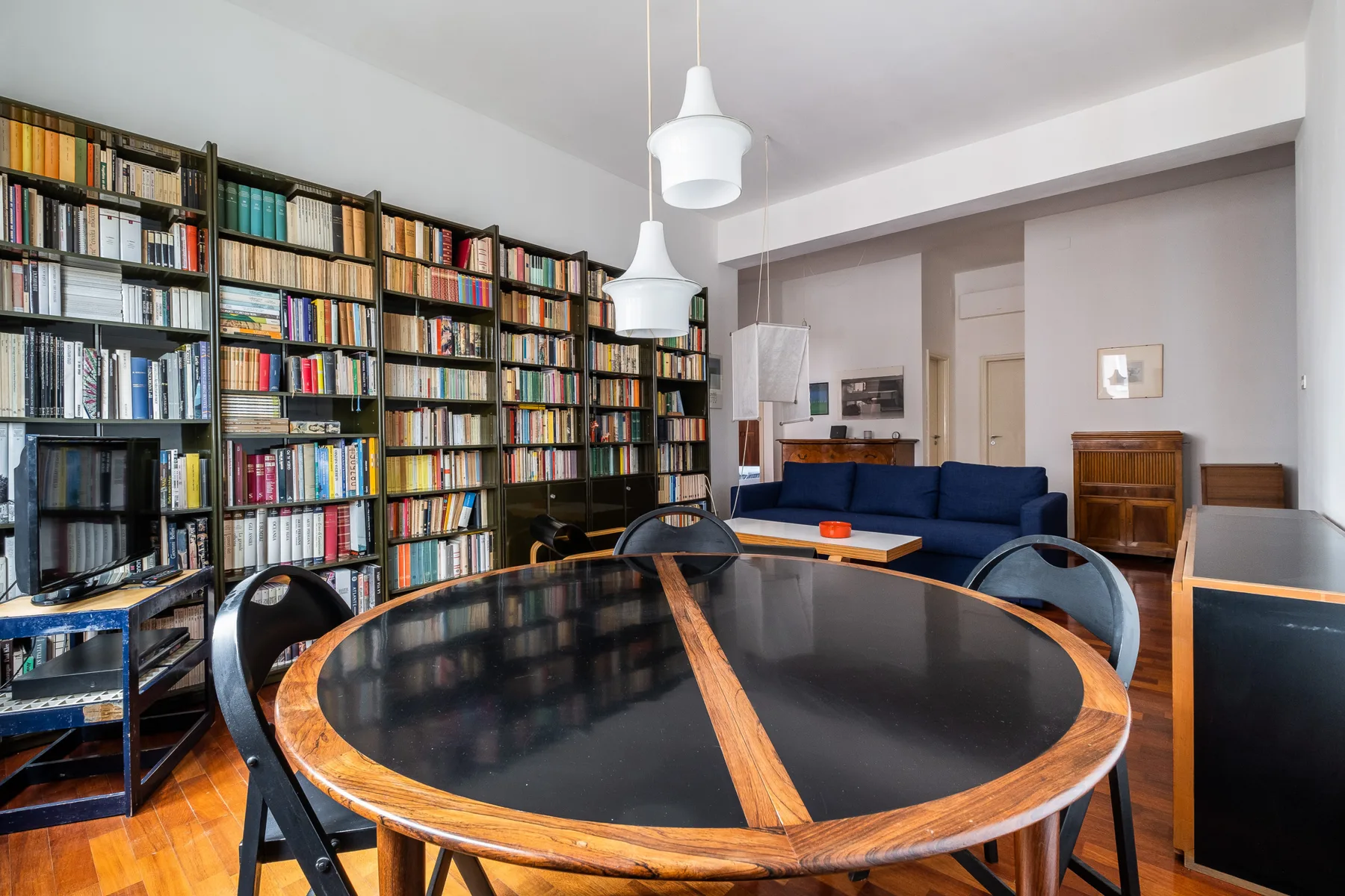 A dining area with a round table, chairs, and bookshelves lining the wall.