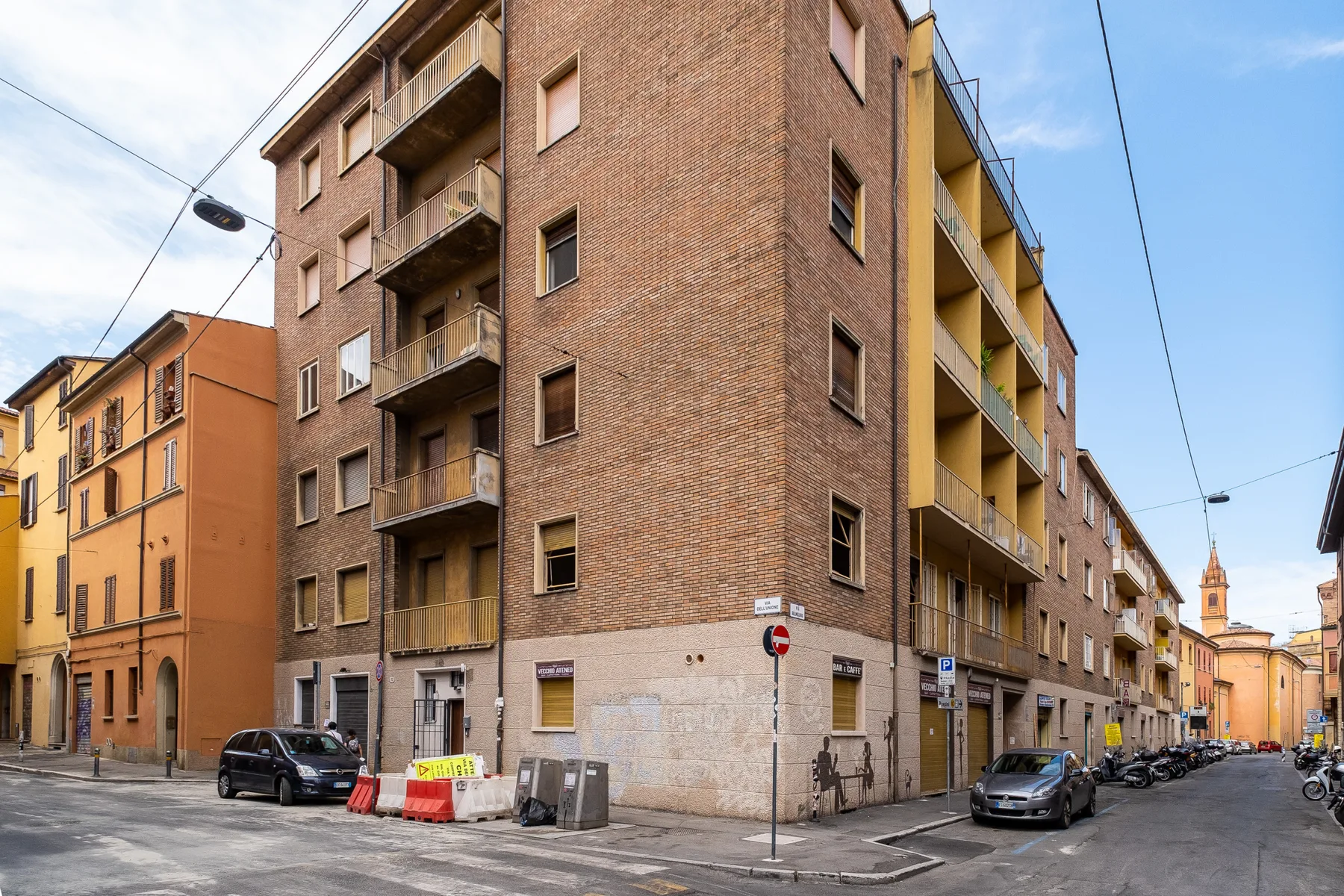 Street corner with a multi-story brick apartment building and parked cars.