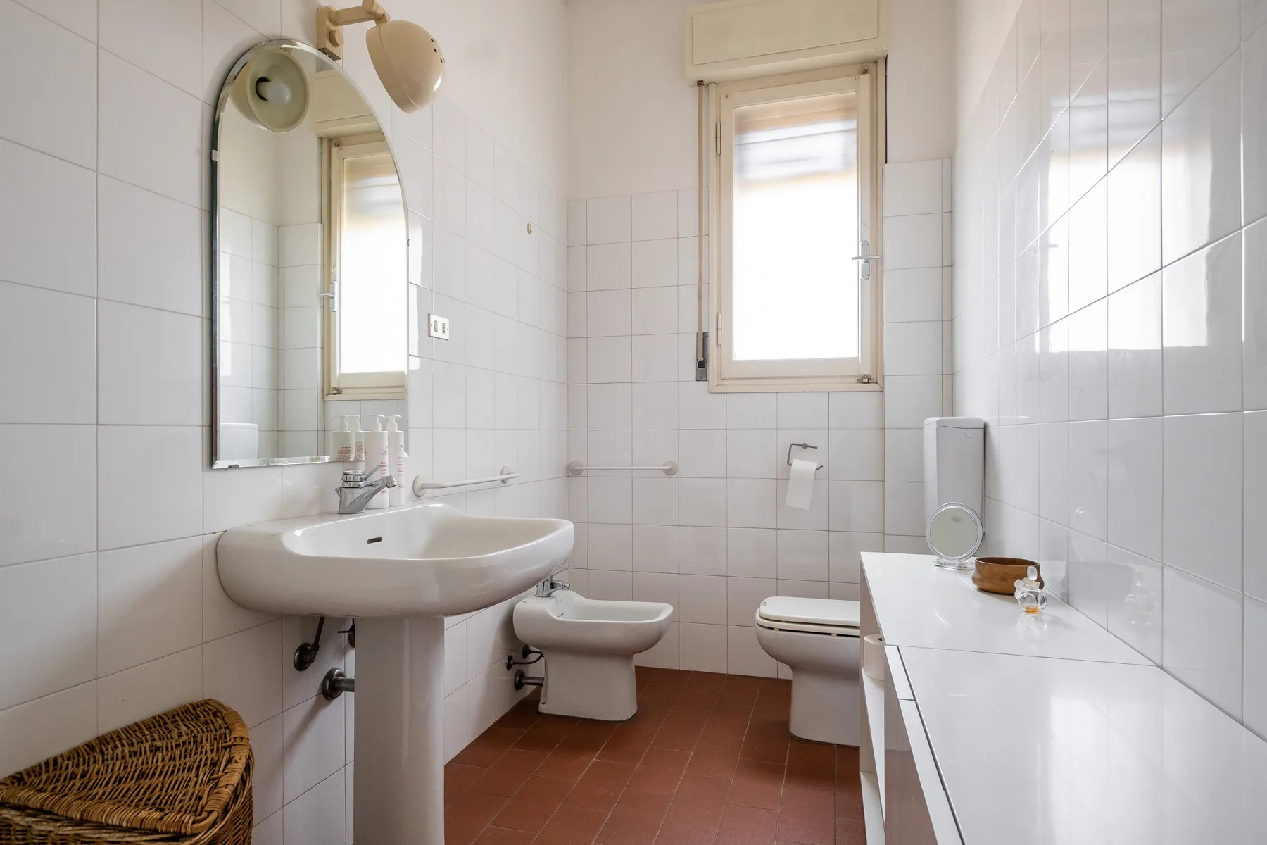 A tiled bathroom with a sink, toilet, and window.