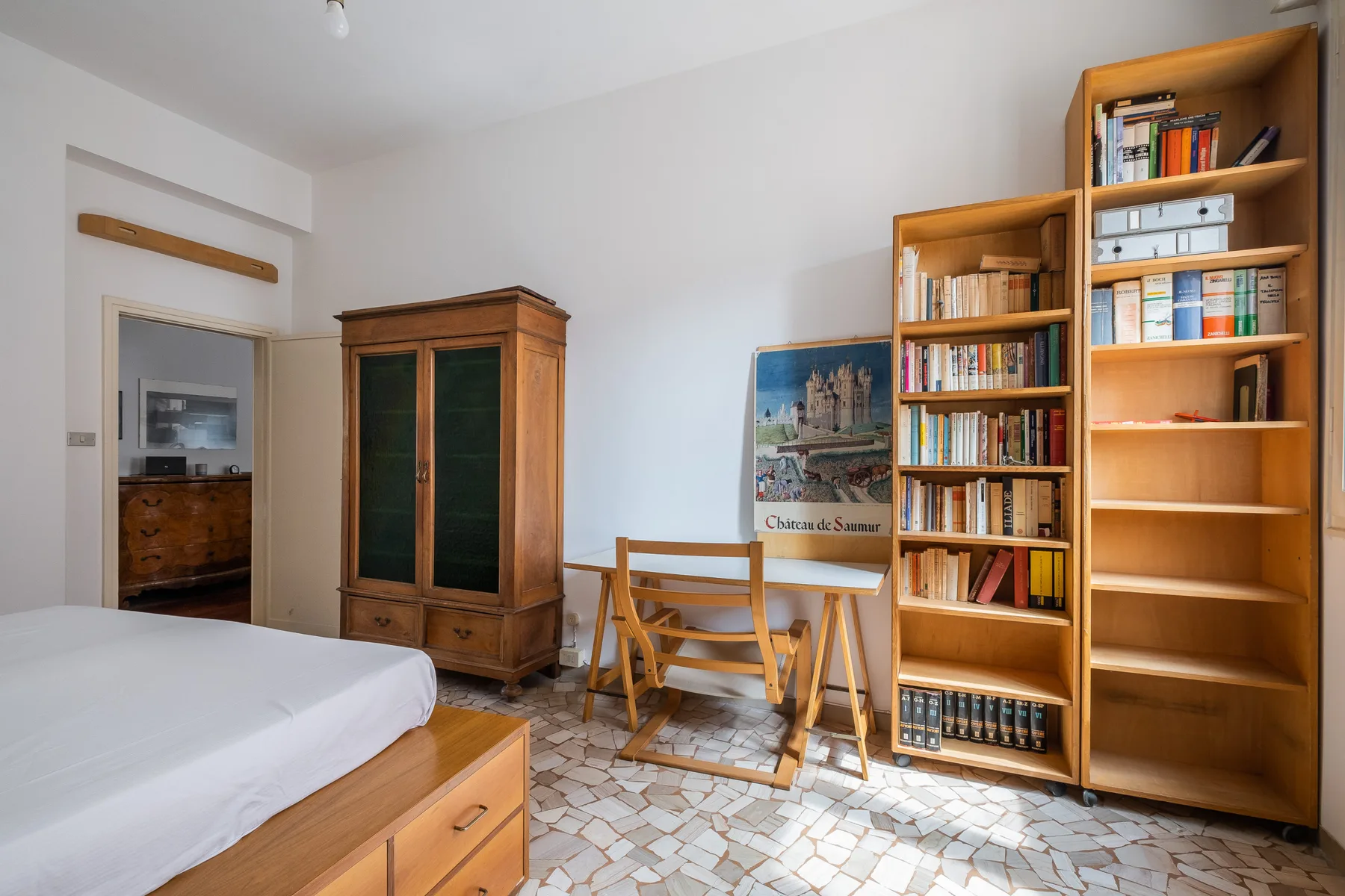 A bedroom with a bed, wooden storage, bookshelves, and a small table.