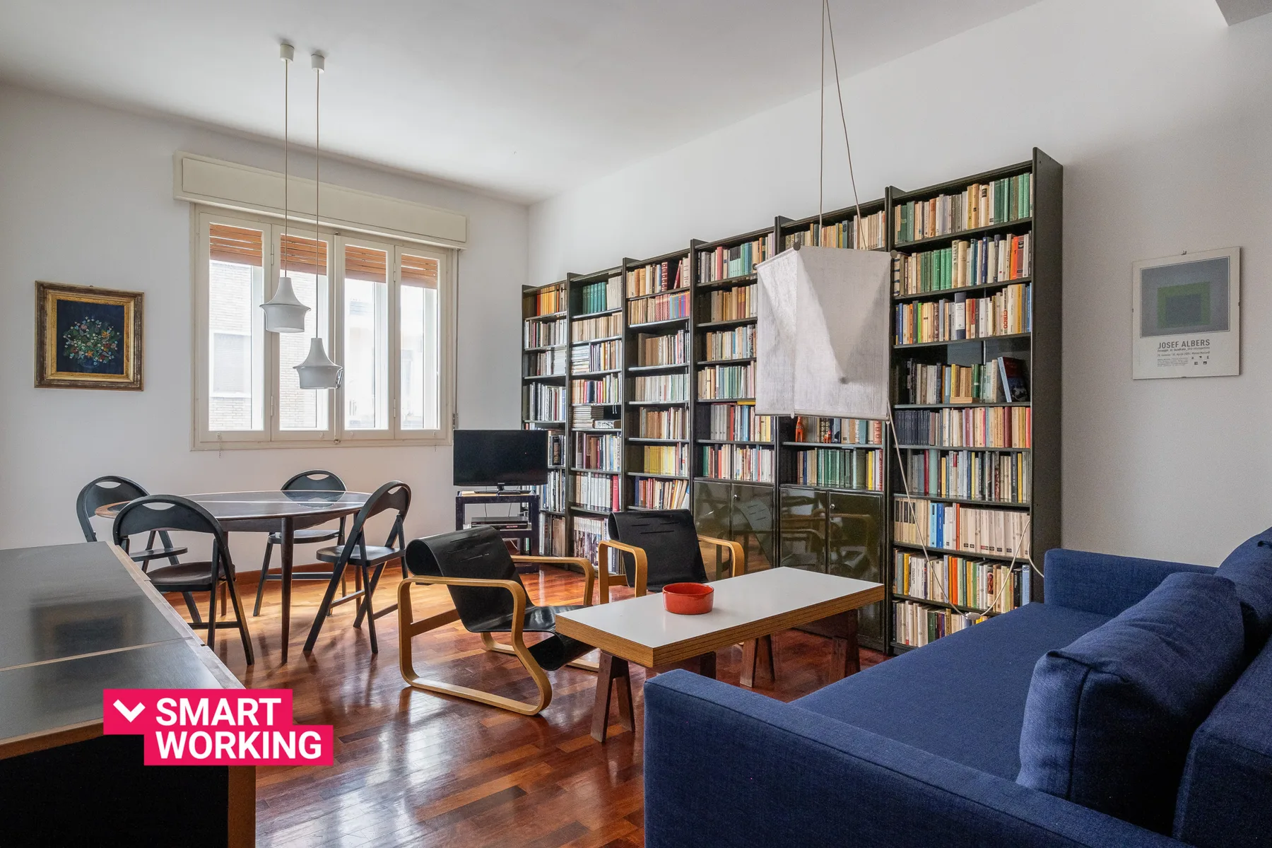 A bright living room with bookshelves, a dining table, and blue seating.