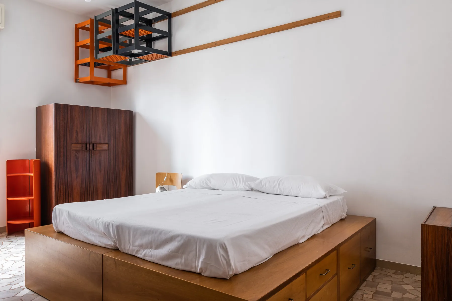 A bedroom with a white bed on a wooden platform and a dark wardrobe.