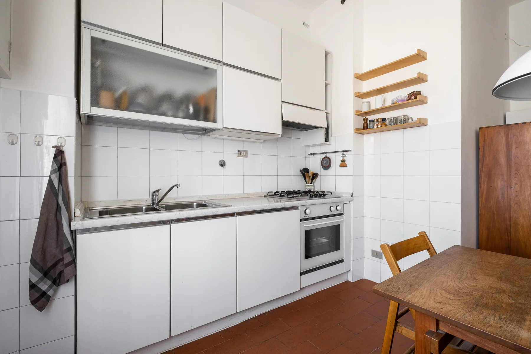 A bright kitchen with white cabinets, a cooking range, and a wooden dining table.