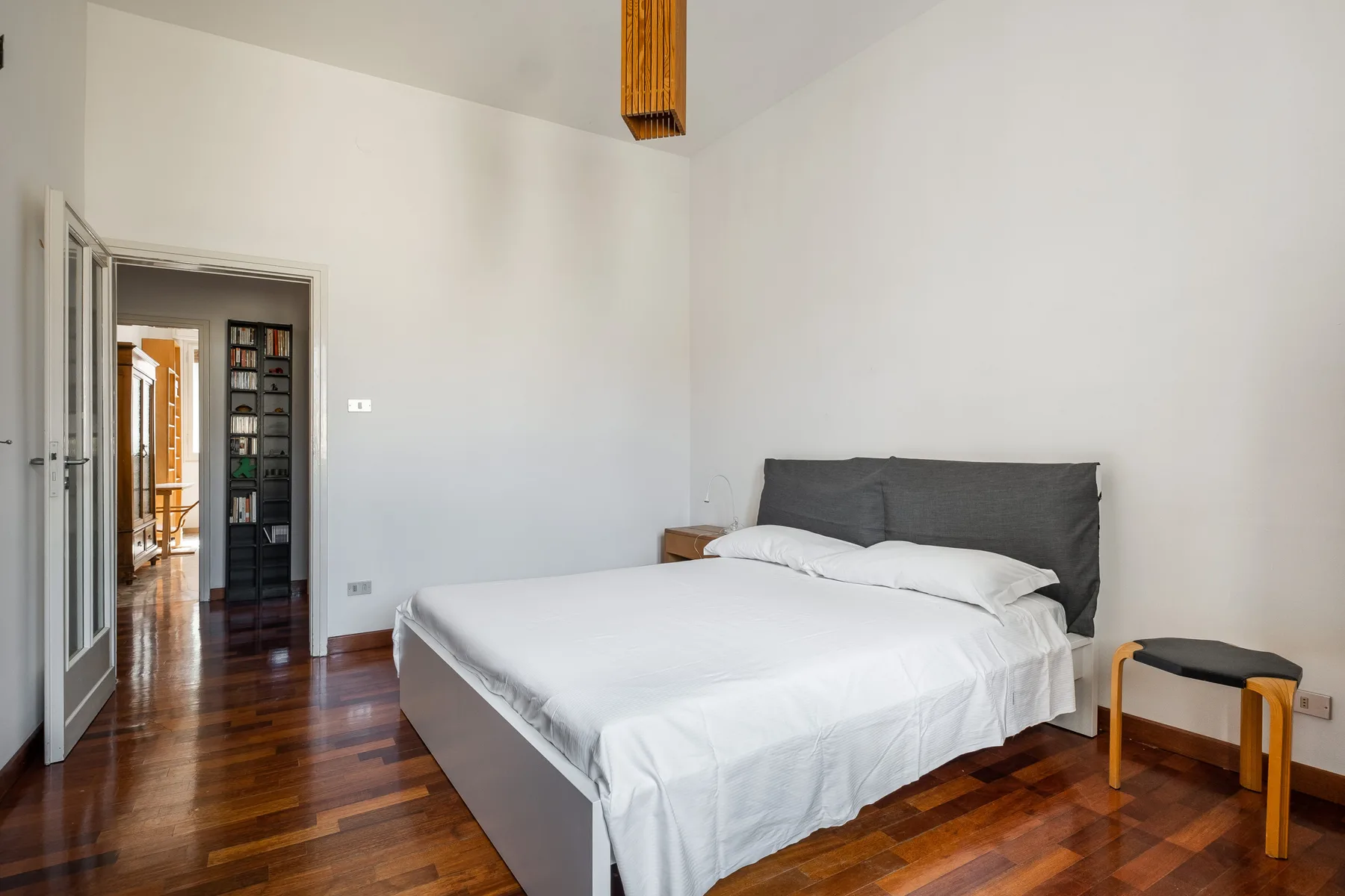A bedroom with a white bed, dark headboard, and polished wood floor.