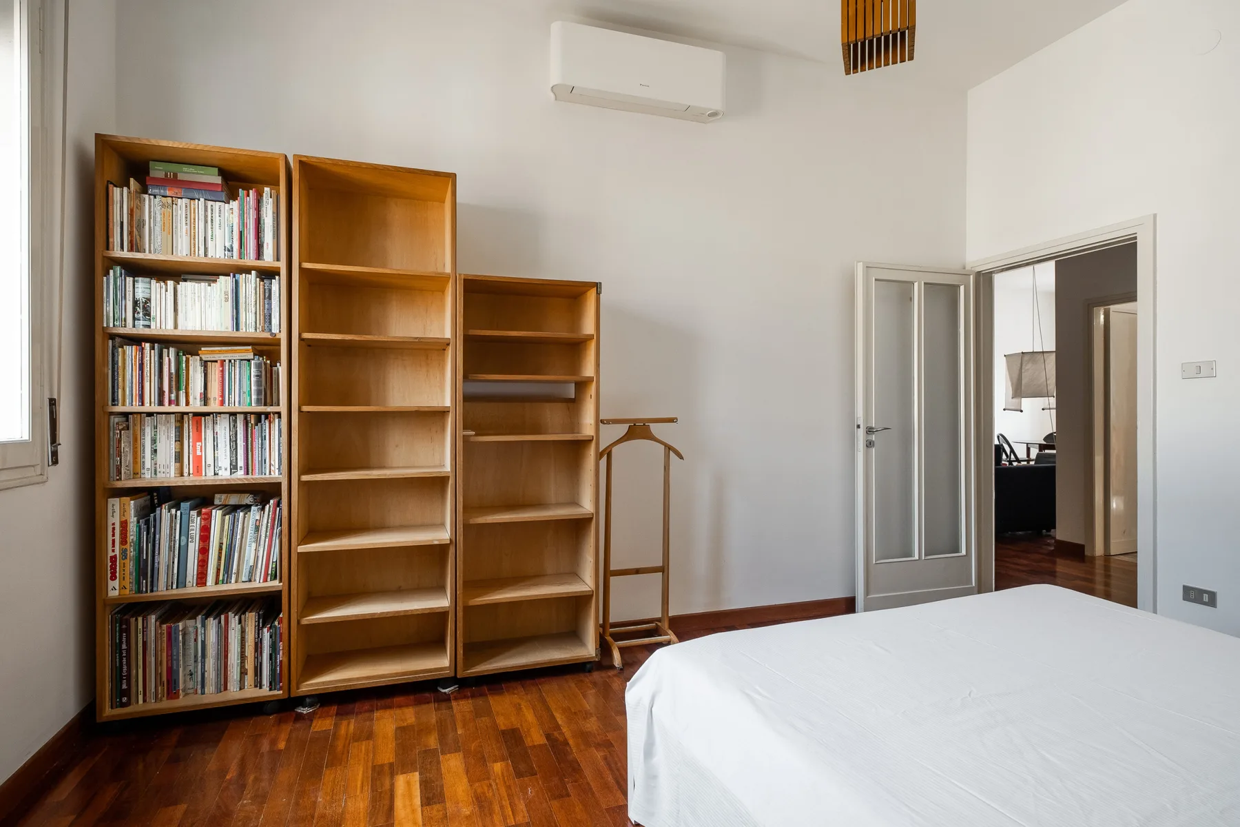 A bedroom with a bed, wooden bookshelves, and an open doorway.