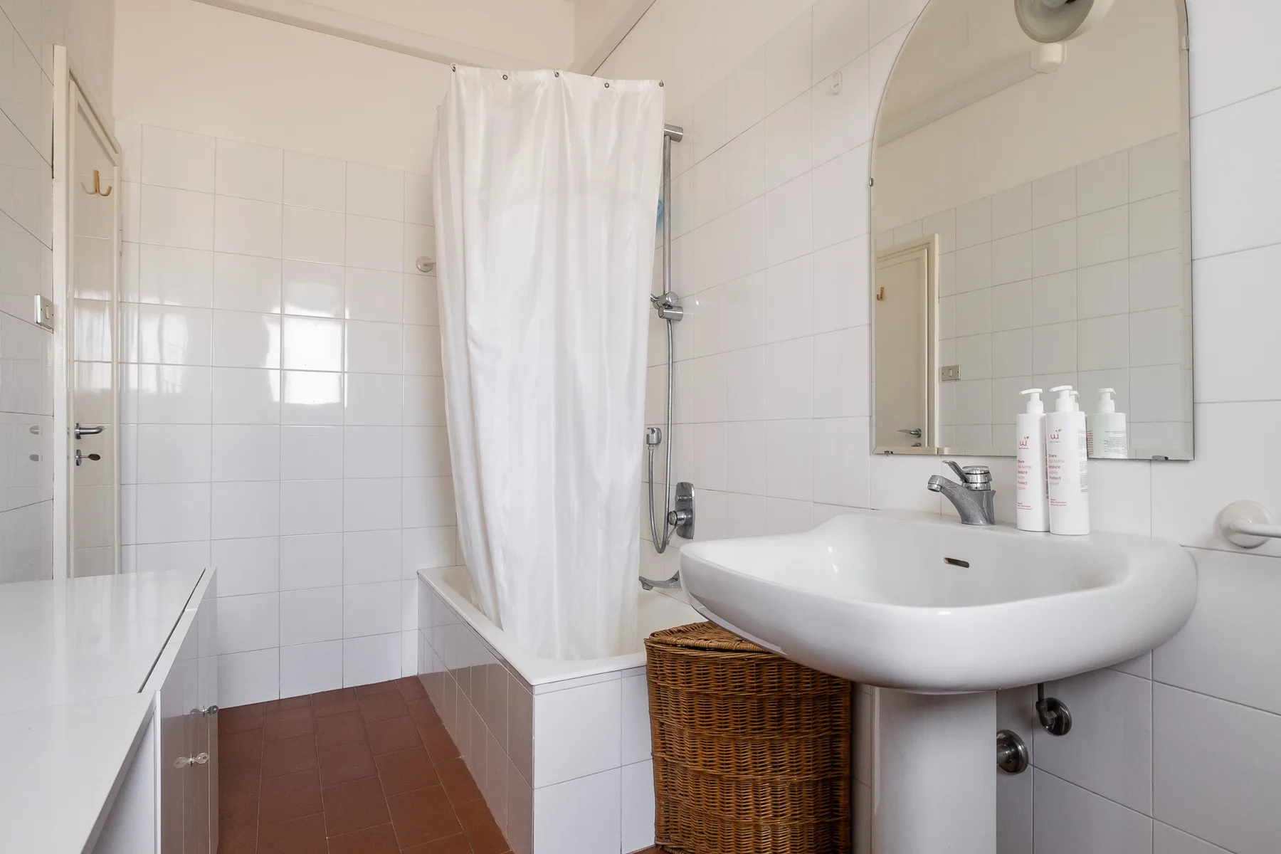 A tiled bathroom with a sink, mirror, and curtained bathtub.