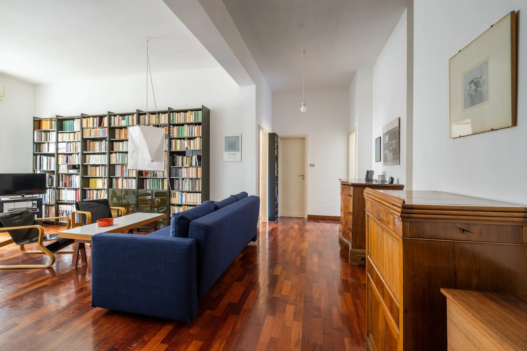 A living room with blue seating, bookshelves, and polished wood flooring.