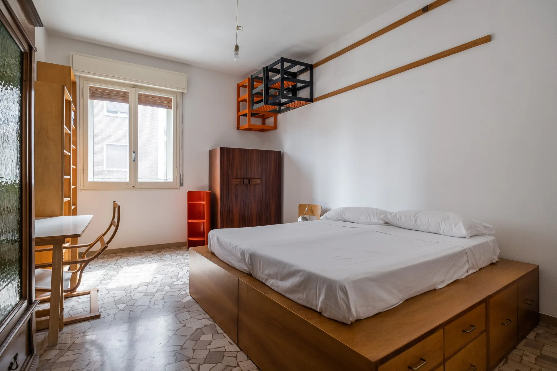 A bedroom with a bed, a window, and a small desk area.