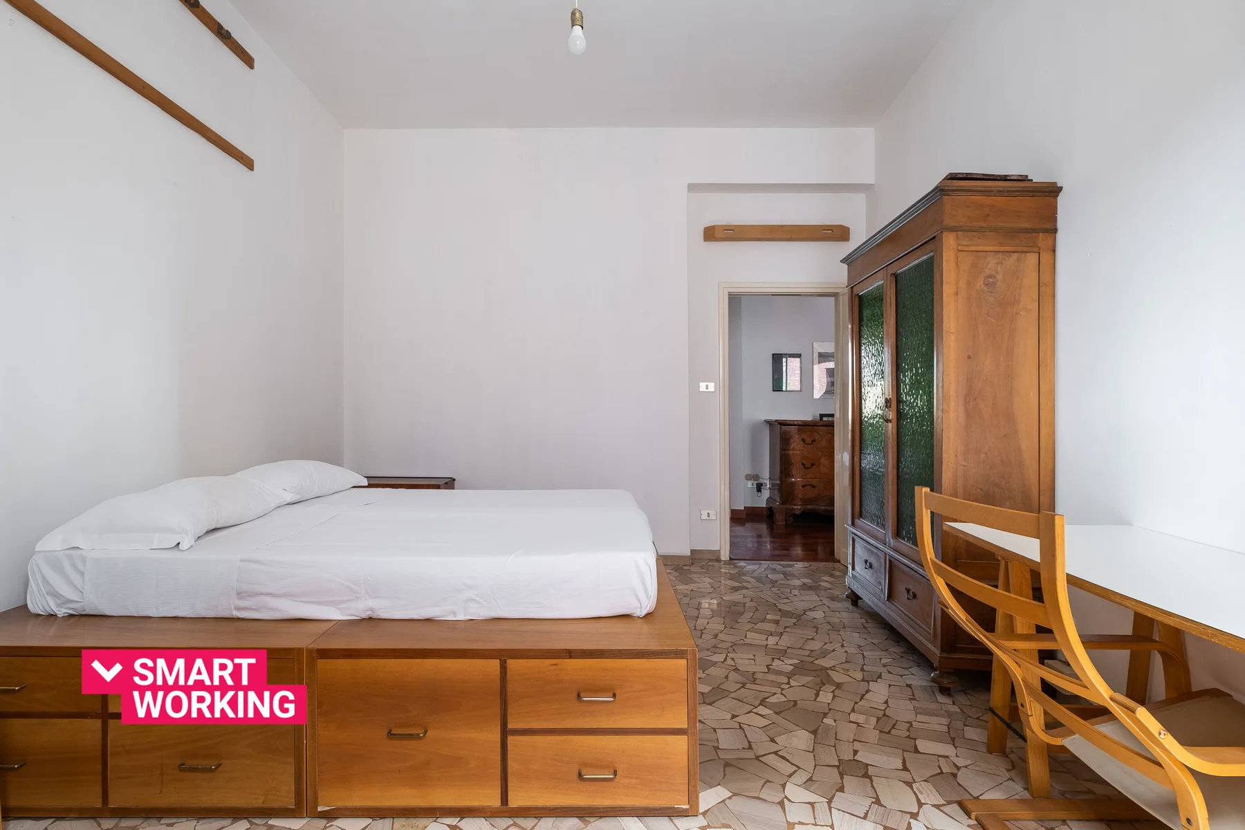 A bedroom with a bed, wooden storage furniture, and a desk.