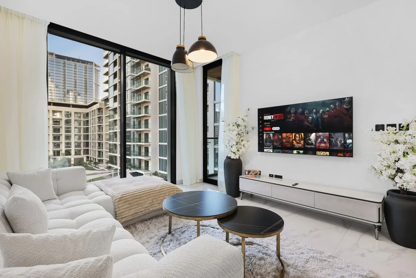 Una sala luminosa con grandes ventanas, asientos y un televisor en la pared.