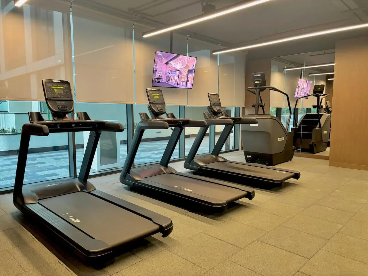 Un gimnasio con cintas de correr y una máquina elíptica junto a grandes ventanales.