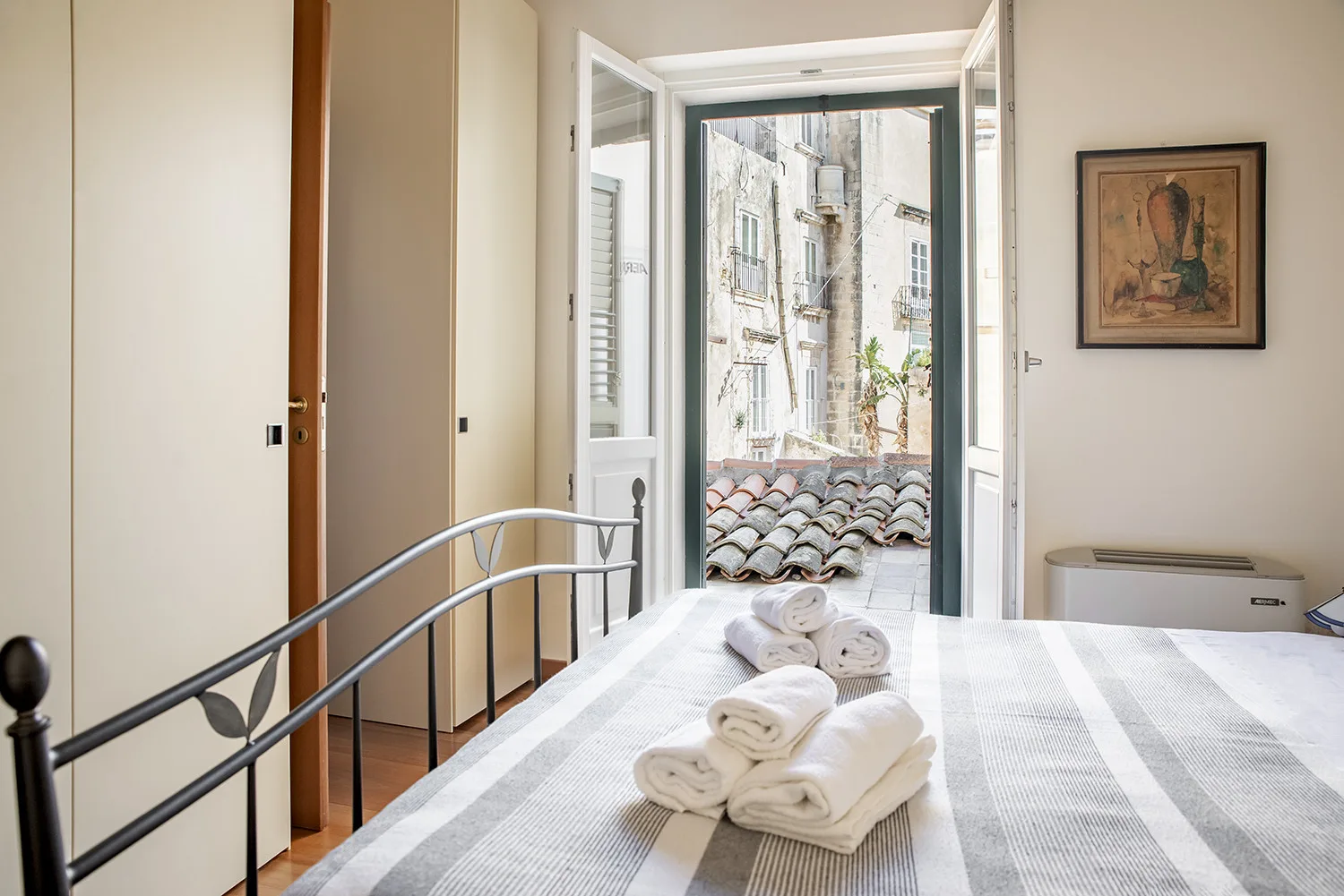 Un dormitorio con la puerta del balcón abierta y toallas dobladas sobre la cama.